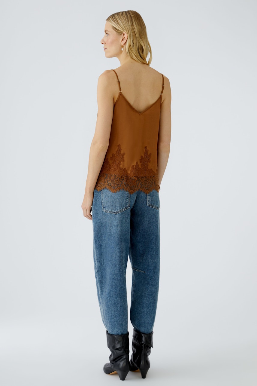 Damen-Top: Junge Frau in braunem Spaghetti-Top mit Spitzenabschluss und lässigen Jeans.