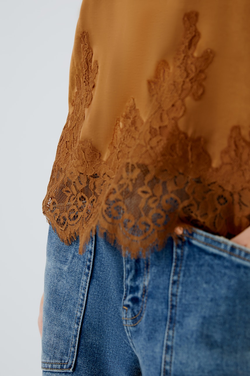 Damen-Top in warmem Braun mit feiner Spitze am Saum, lässig kombiniert mit Jeans.