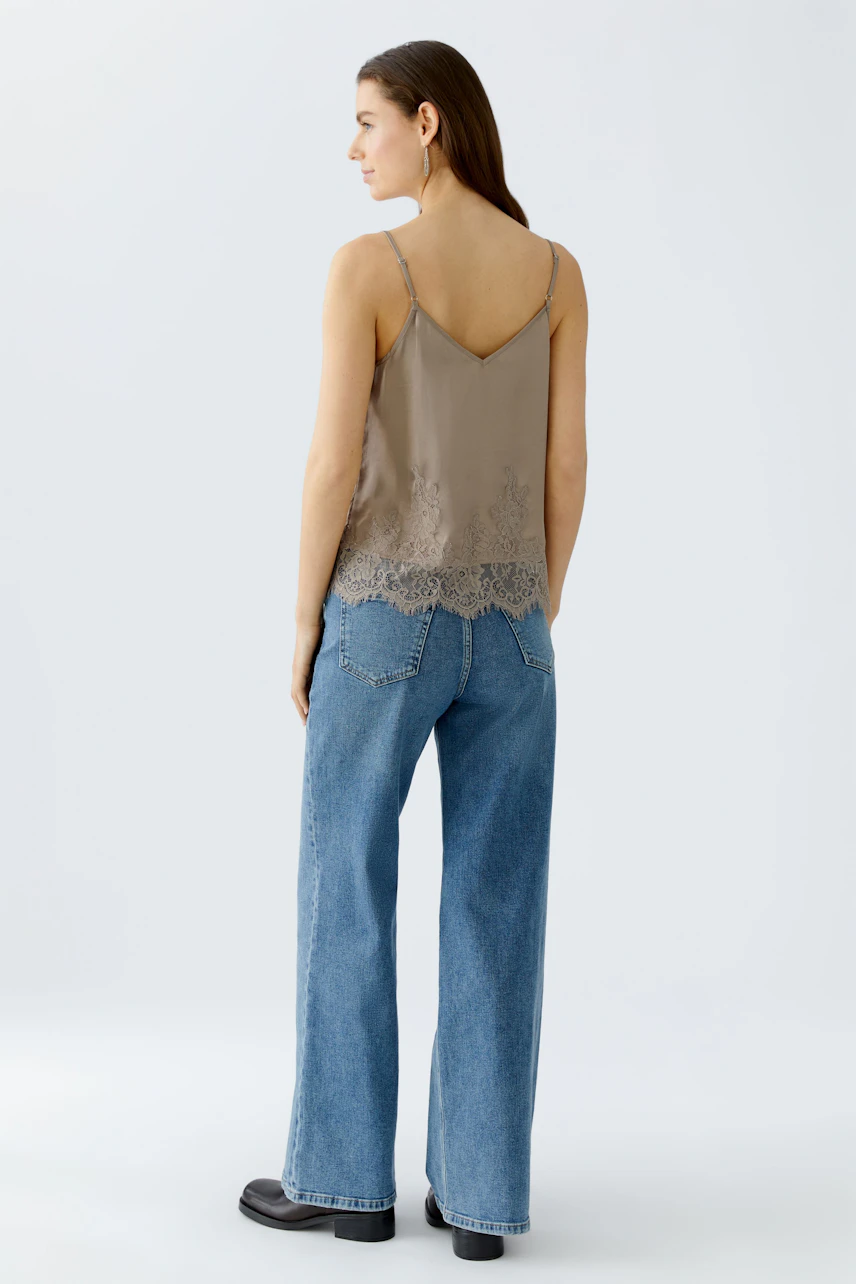 Casual women's top: Young woman in a beige lace-trimmed tank top and wide-leg jeans.