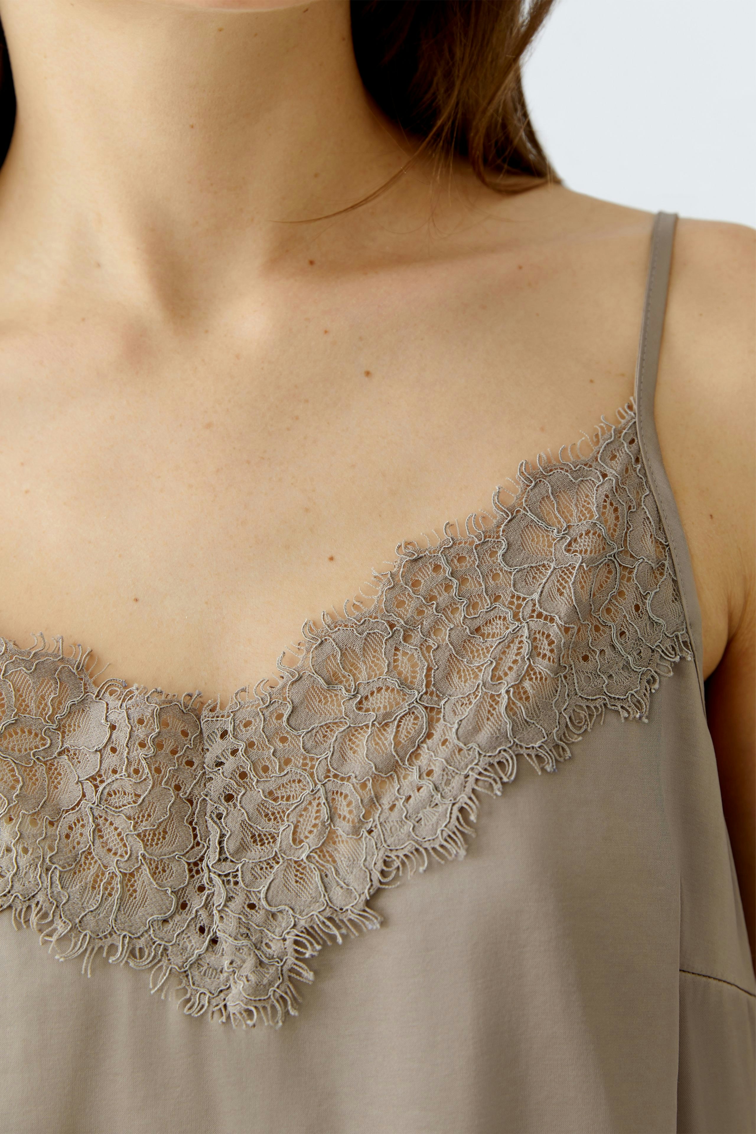 Casual women's top: Close-up of a woman wearing a light brown top with lace detailing.