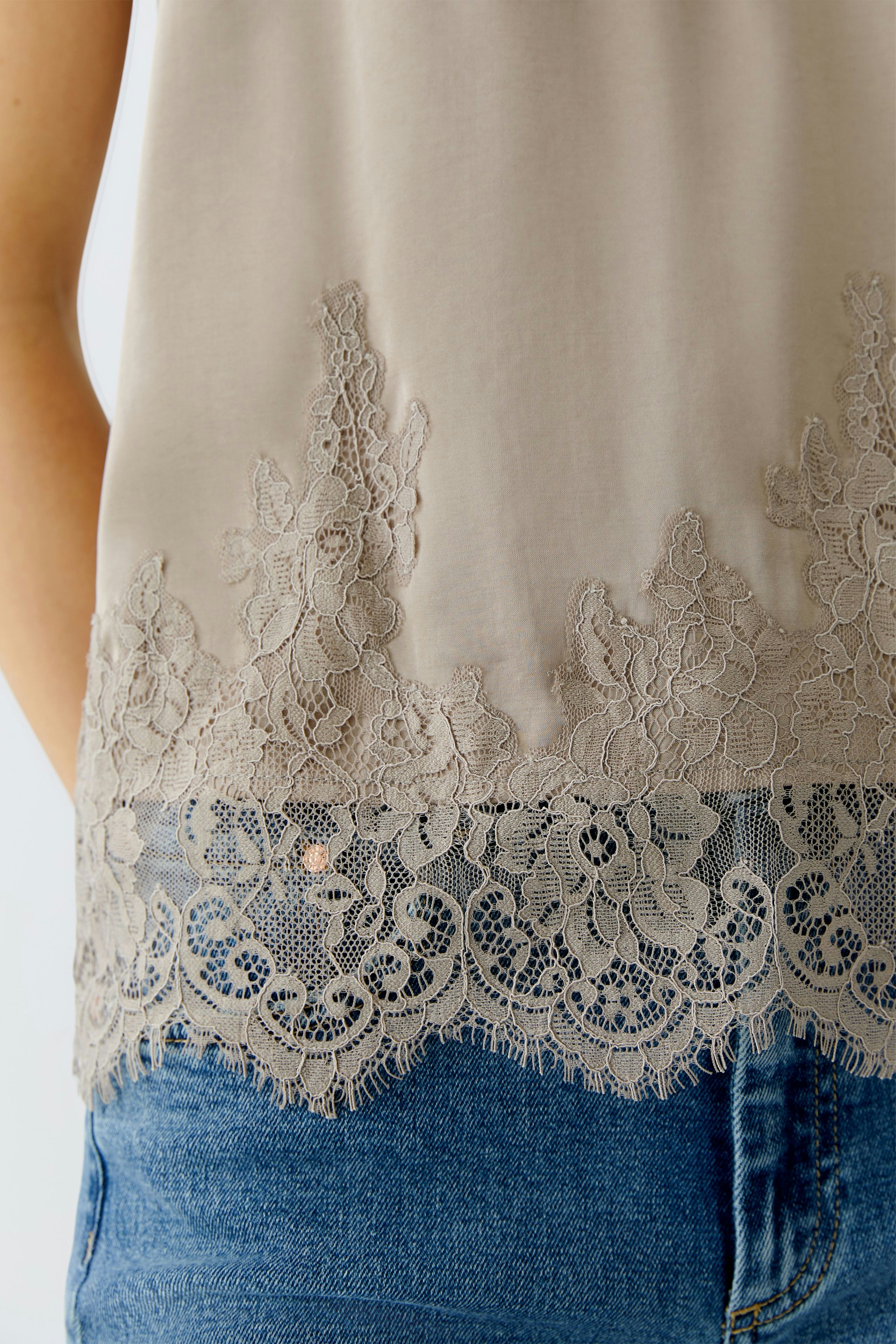 Casual women's top: Close-up of a woman wearing a light beige top with lace detailing and denim shorts.