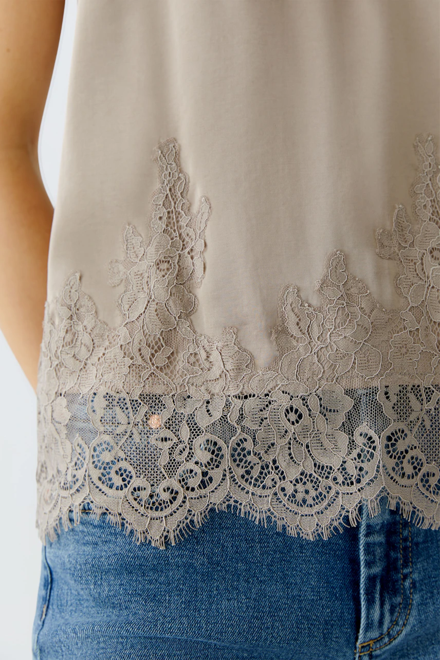 Casual women's top: Close-up of a woman wearing a light beige top with lace detailing and denim shorts.