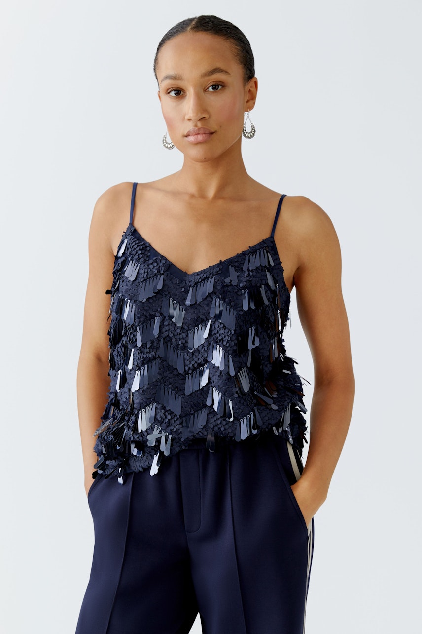 Stylish women's top: A woman in a navy sequined top with thin straps, paired with relaxed trousers.