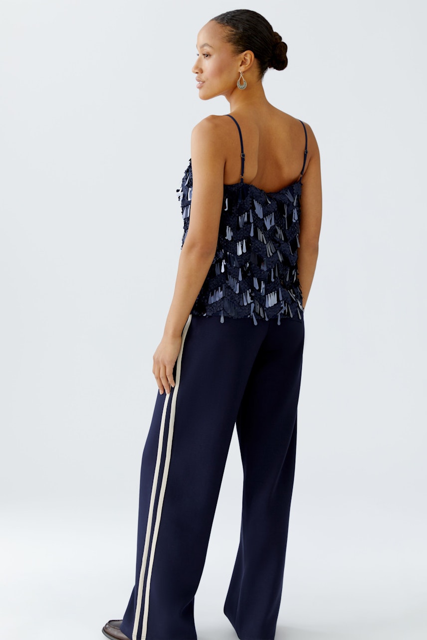 Stylish women's top: A woman in a navy sequined top with thin straps, paired with wide-leg pants.
