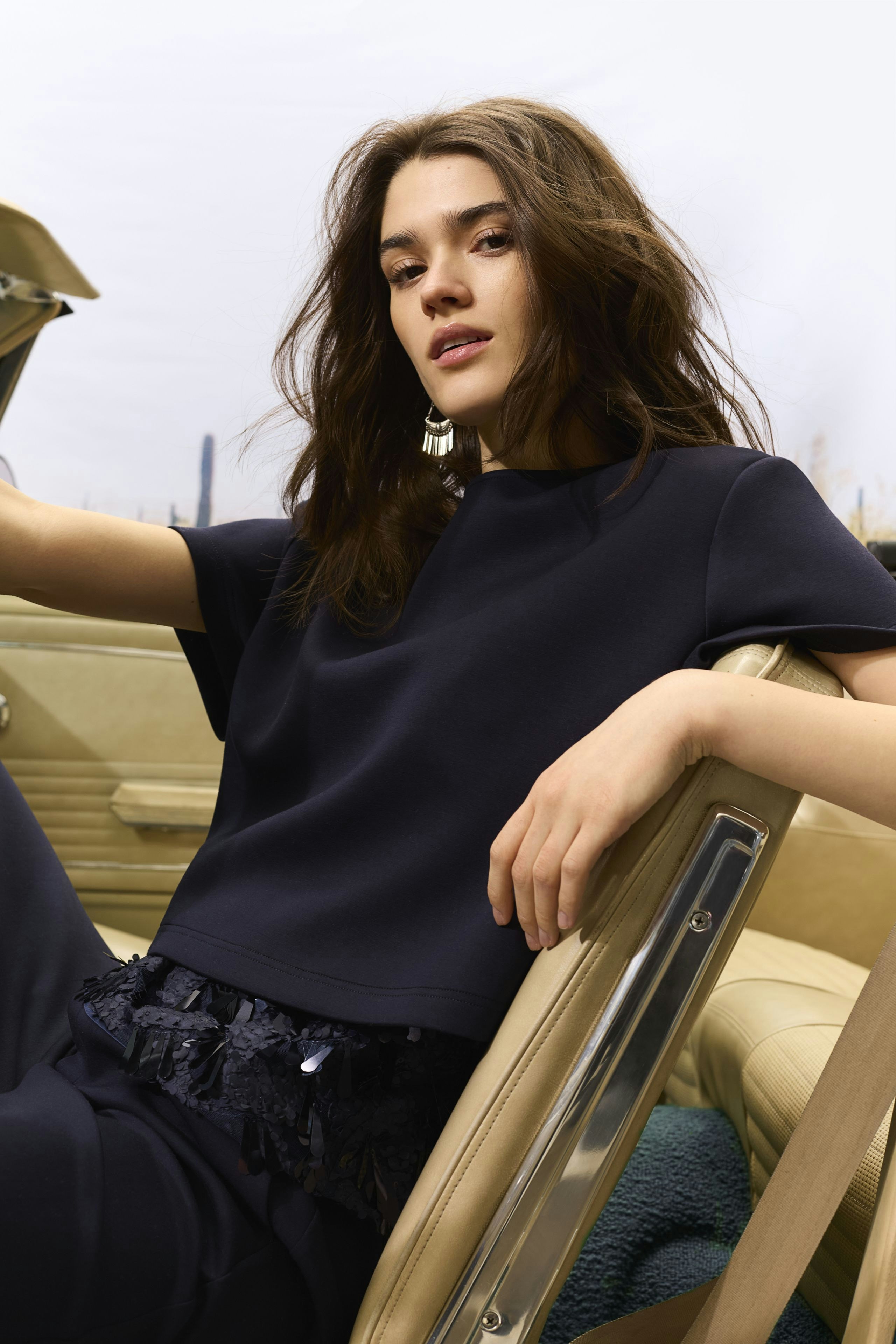 Damen-Top: Junge Frau in einem navyfarbenen Top mit fransigem Saum sitzt entspannt im Auto.