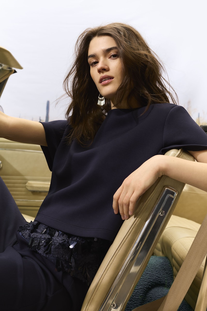 Casual women's top: Young woman in a navy top with fringe detail, sitting confidently in a car.