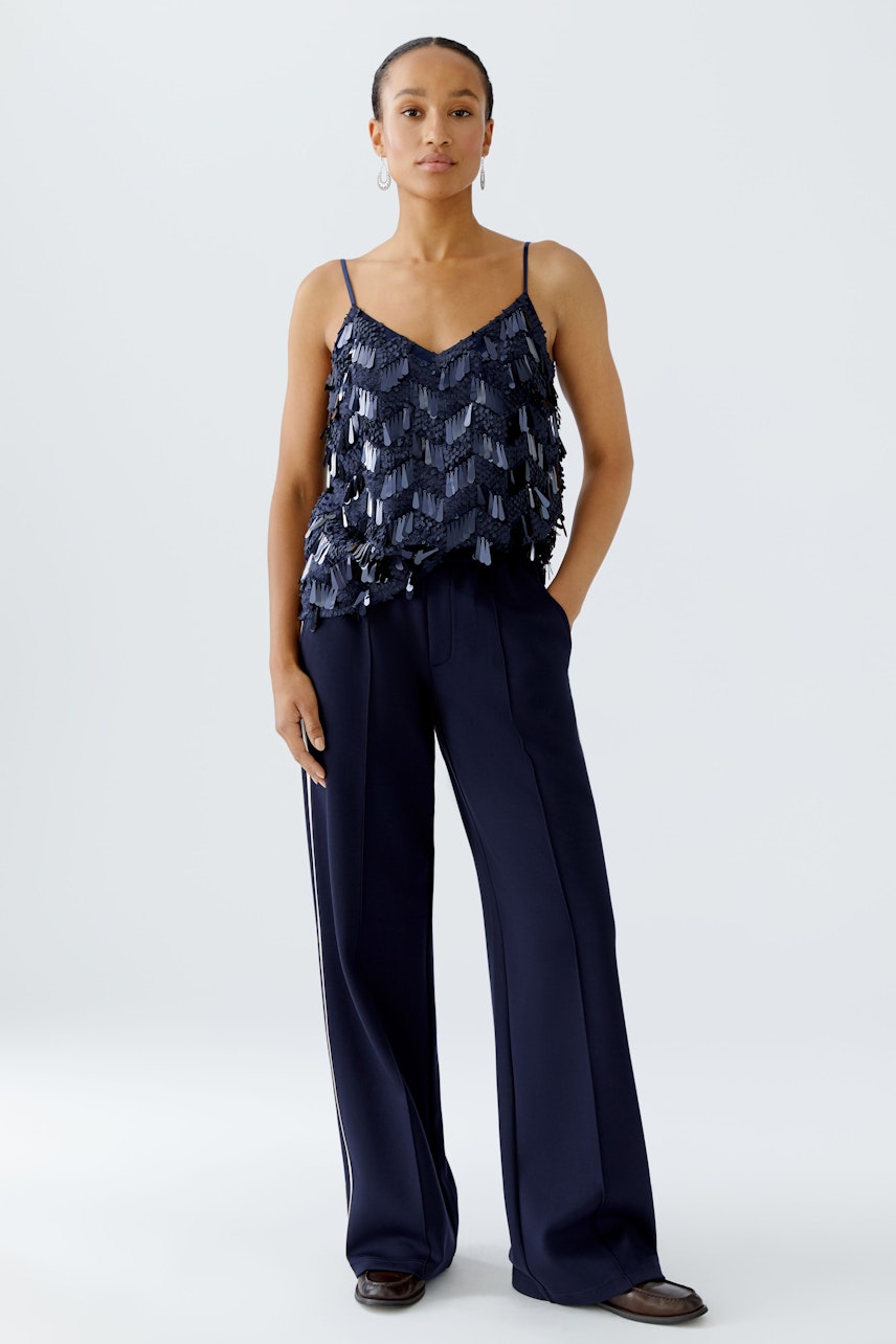 Stylish women's top: A woman in a navy top with layered details and wide-leg pants stands confidently.