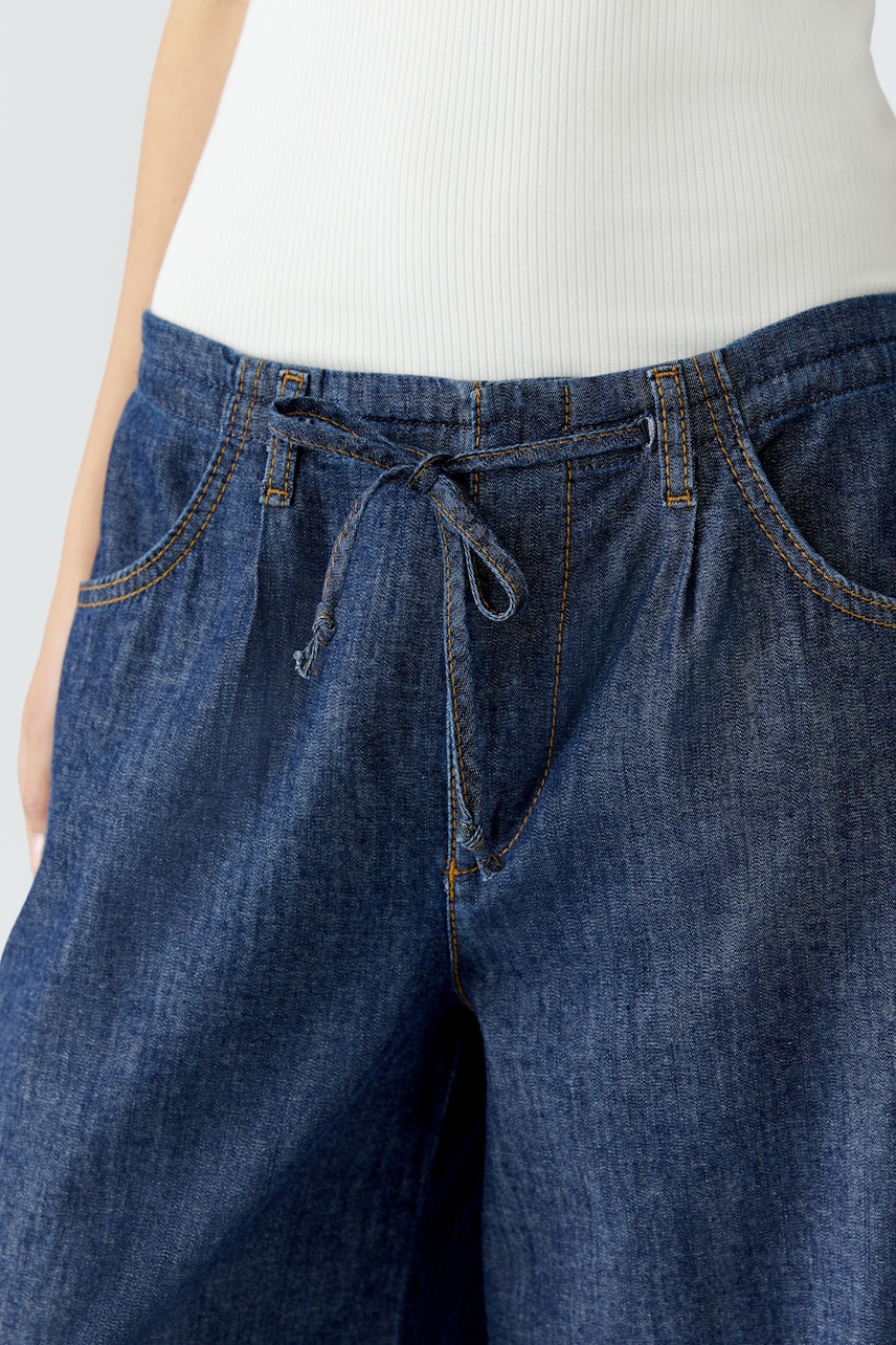 Wide leg jeans: Woman wearing dark blue wide leg jeans with a drawstring waist for a relaxed fit.