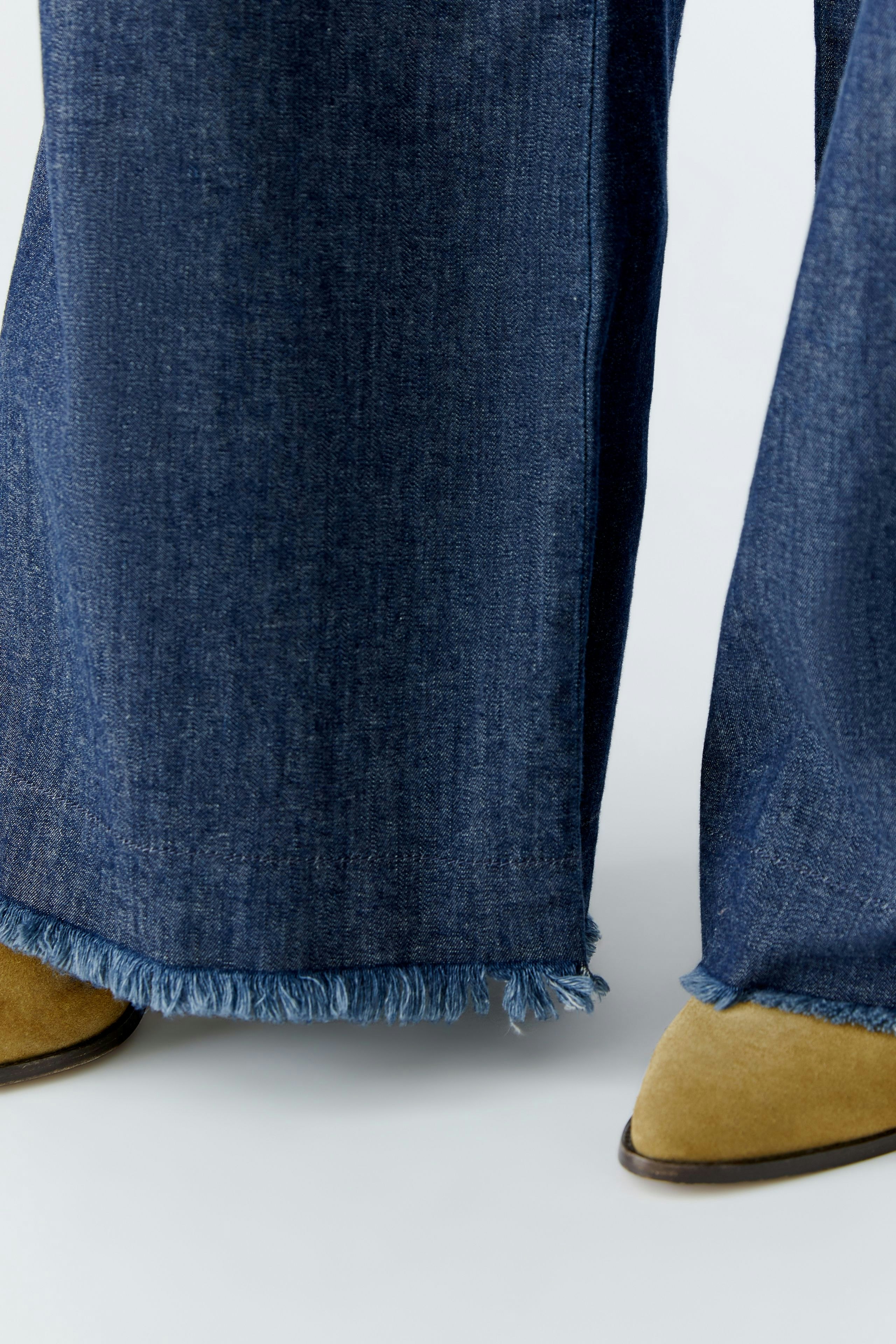 Wide leg jeans: A woman wearing dark blue wide leg jeans with frayed hems and stylish boots.