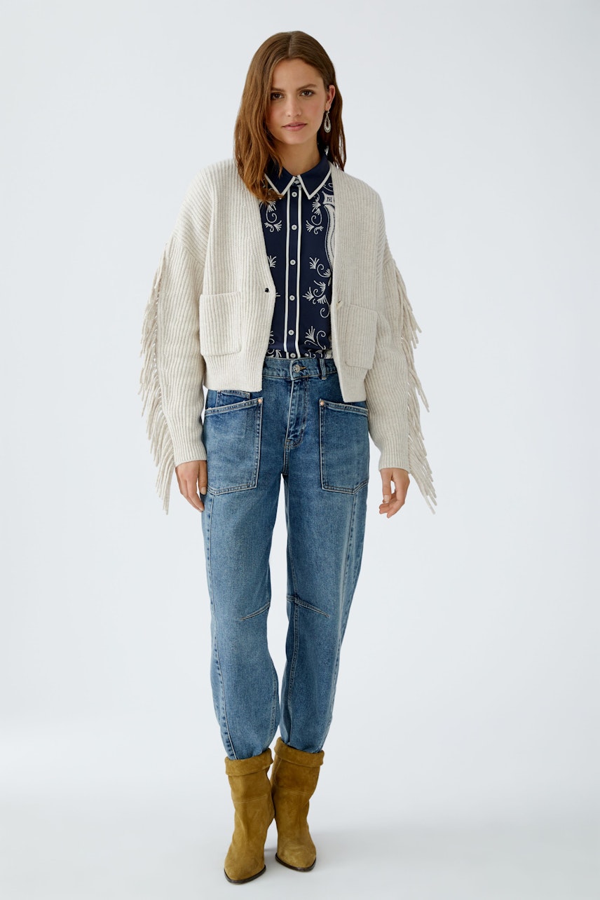 Casual women's jeans barrel: A woman in relaxed-fit jeans with a stylish top and fringe cardigan.