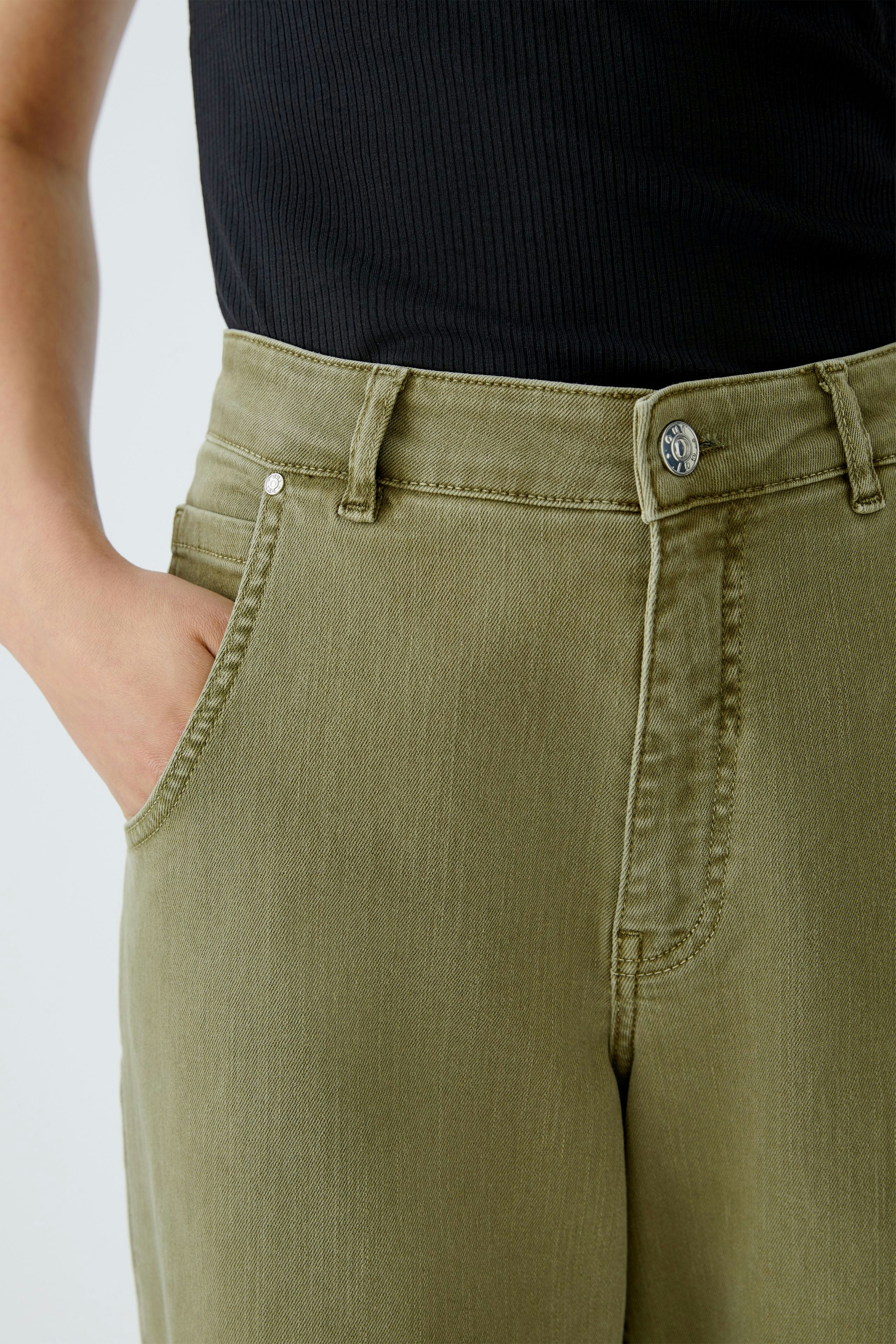 Casual women's jeans: Close-up of a woman wearing olive green barrel jeans with a fitted top.