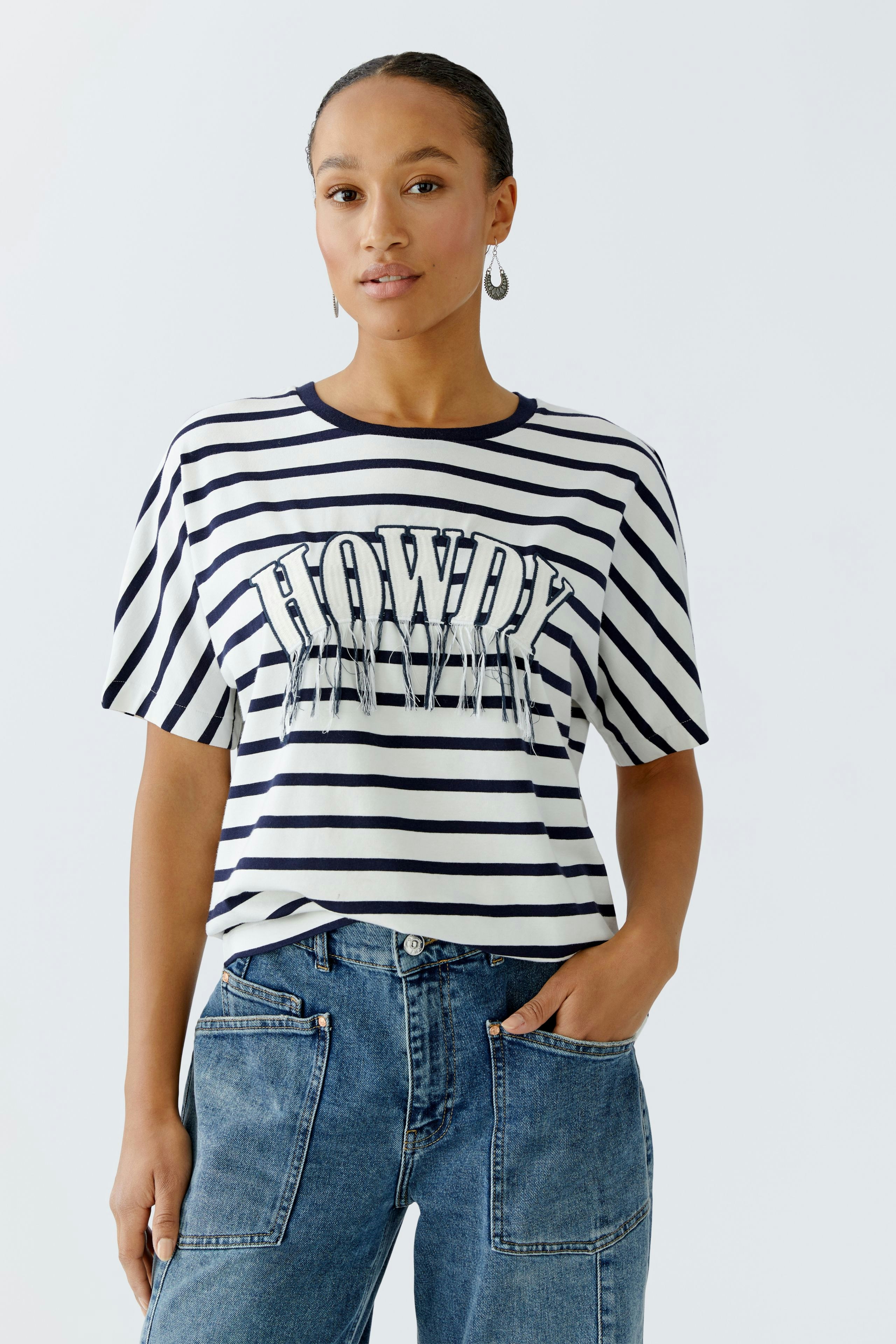 Casual women's T-shirt: Young woman in a striped tee with 'Howdy' print, paired with relaxed jeans.