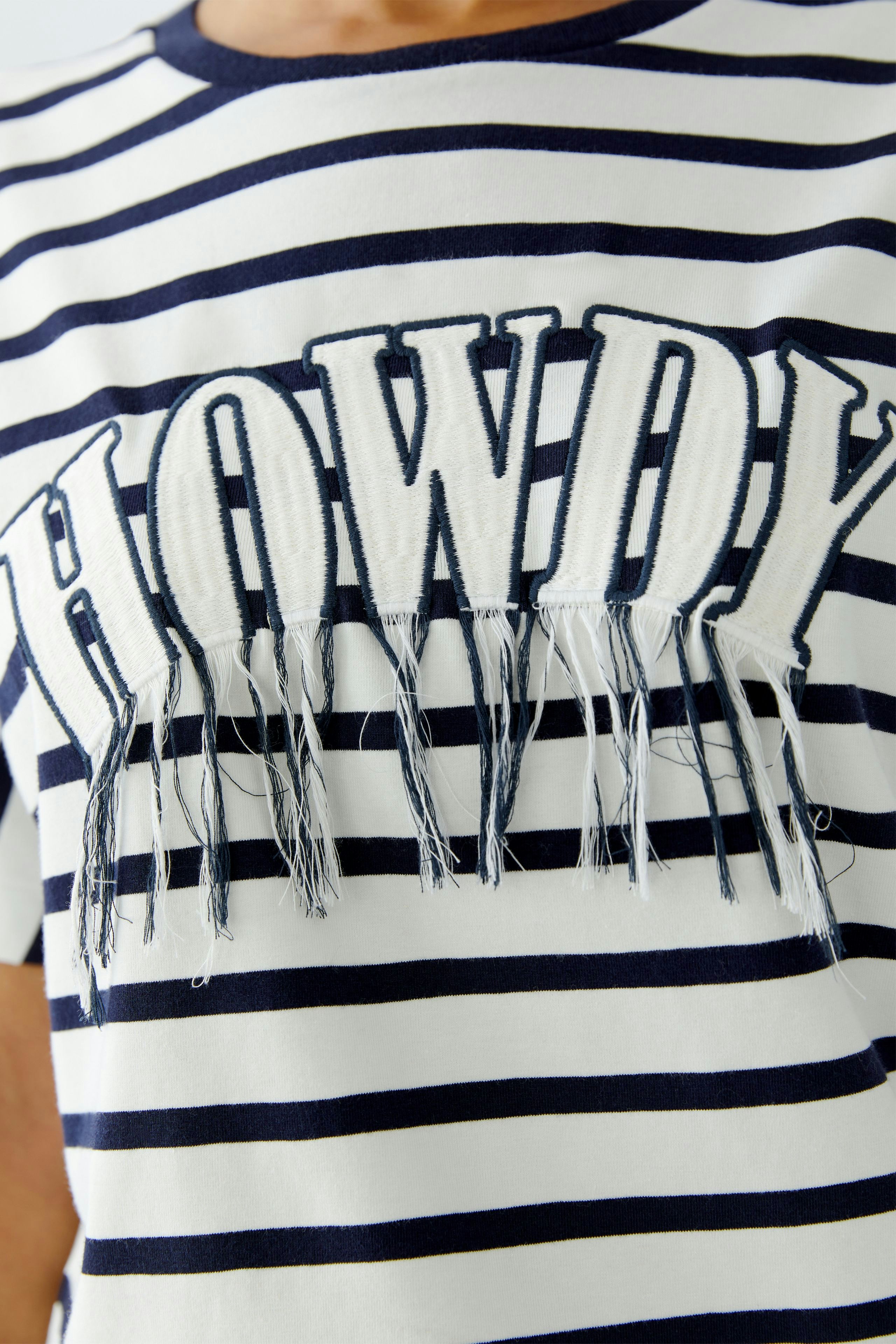 Casual women's T-shirt: Close-up of a woman in a striped tee with 'HOWDY' and fringe details.