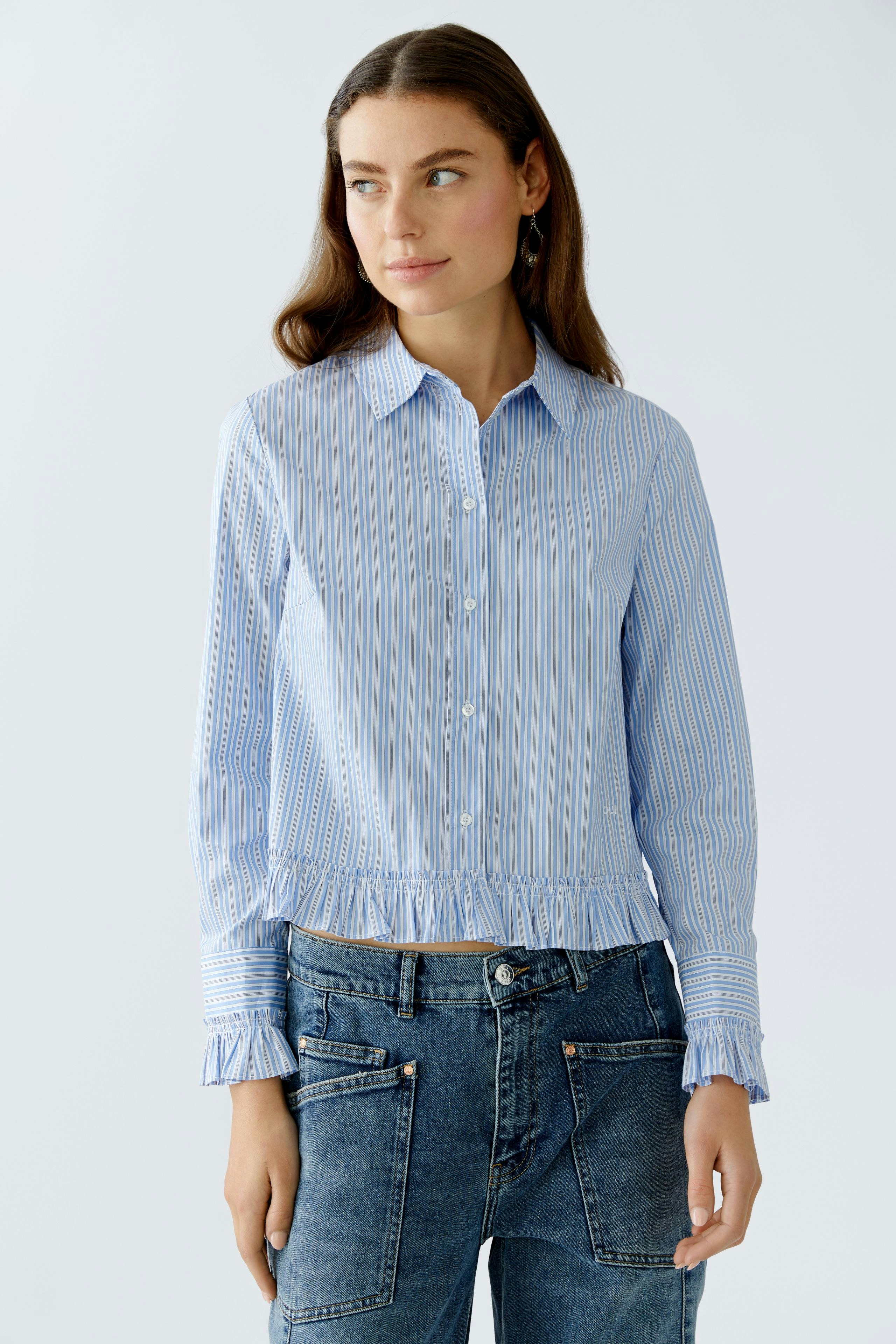 Casual women's blouse: Young woman in a blue striped blouse with ruffled hem and relaxed jeans.