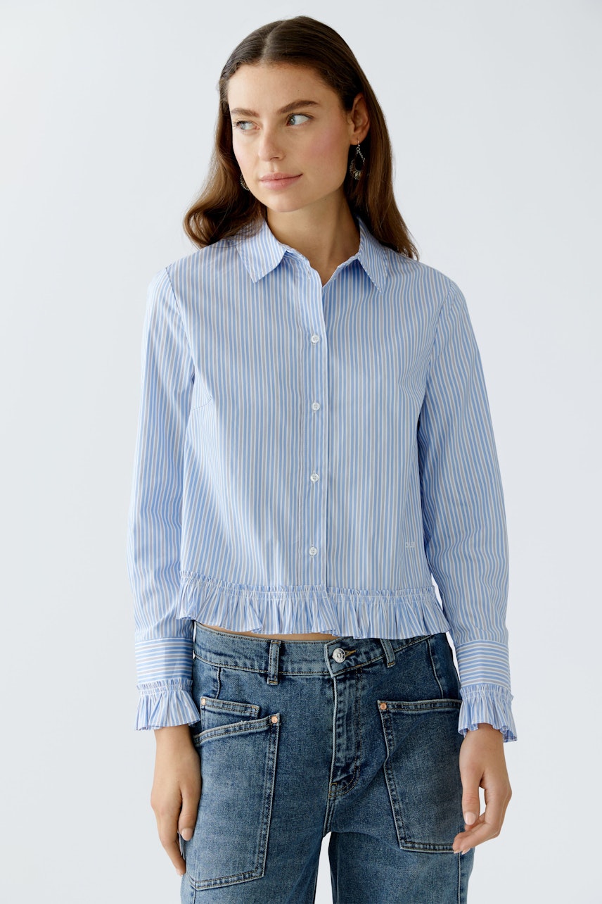 Casual women's blouse: Young woman in a blue striped blouse with ruffled hem and relaxed jeans.