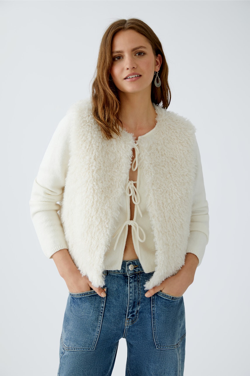 Casual women's vest: A woman in a fluffy, color-blocked vest over a knitted pullover and jeans.
