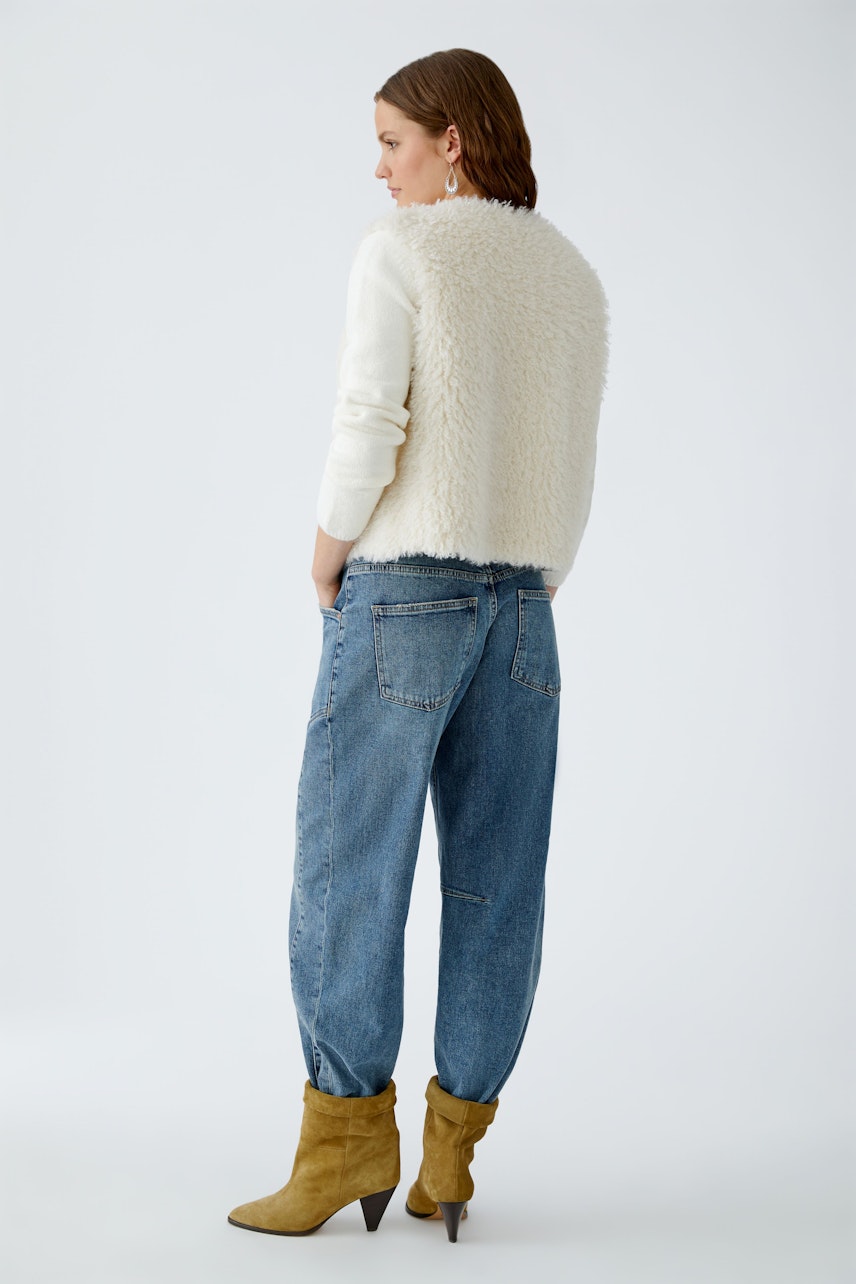 Cozy women's vest: A woman in a fluffy vest with colorful sleeves, paired with relaxed jeans.