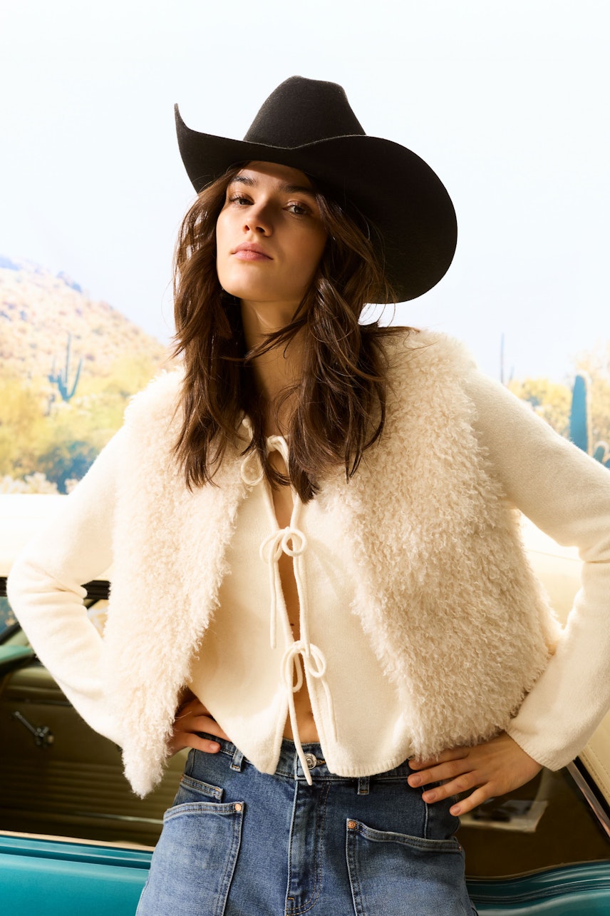 Casual women's vest: A woman in a fluffy cream vest with a tie front, paired with denim jeans.