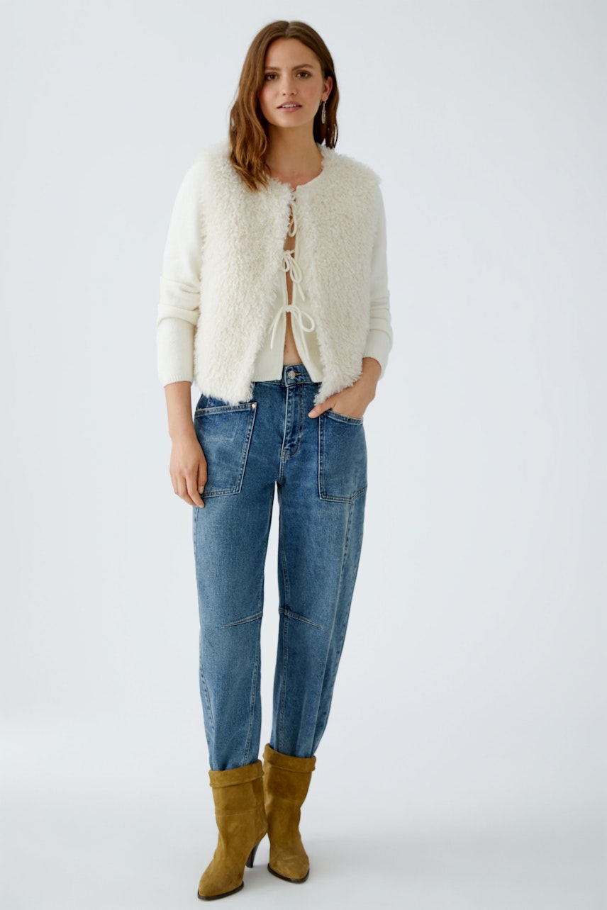 Cozy women's vest: A woman in a fluffy vest over a striped pullover, paired with relaxed jeans.