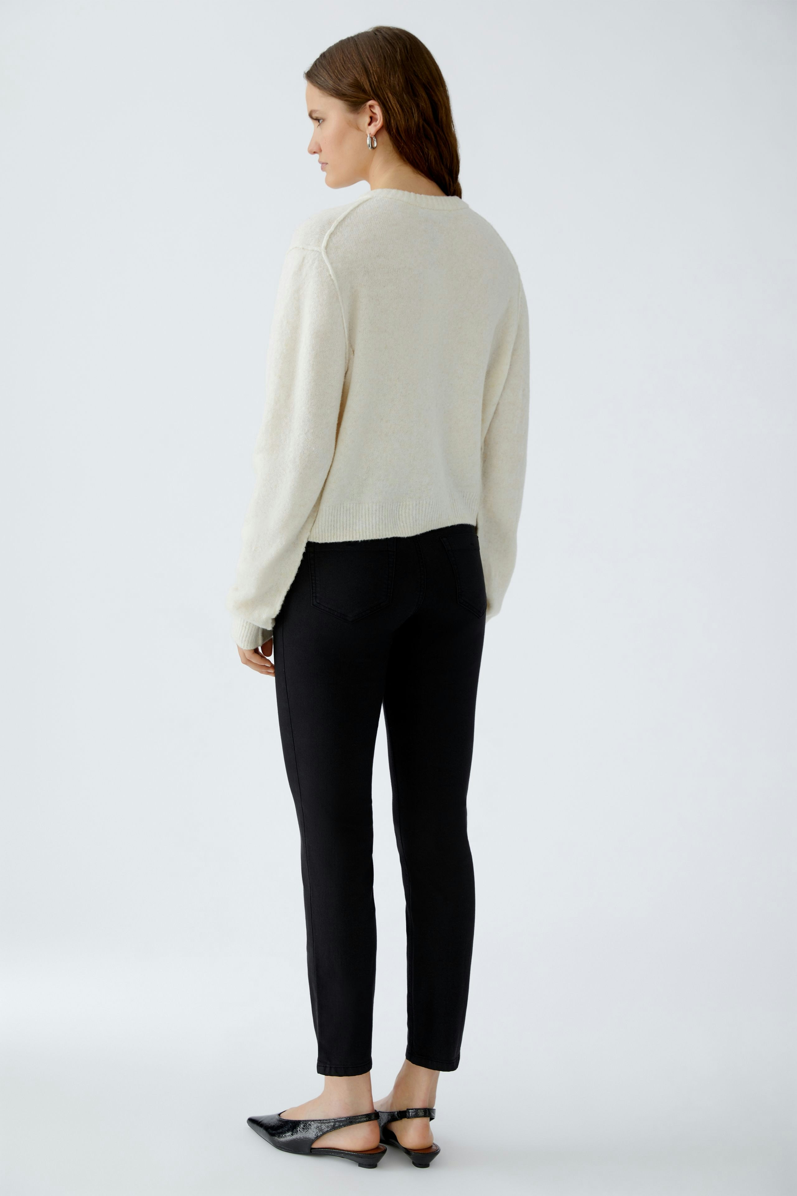 Bequeme Damen-Strickjacke: Frau in cremefarbener Strickjacke und schwarzen Jeans von hinten.