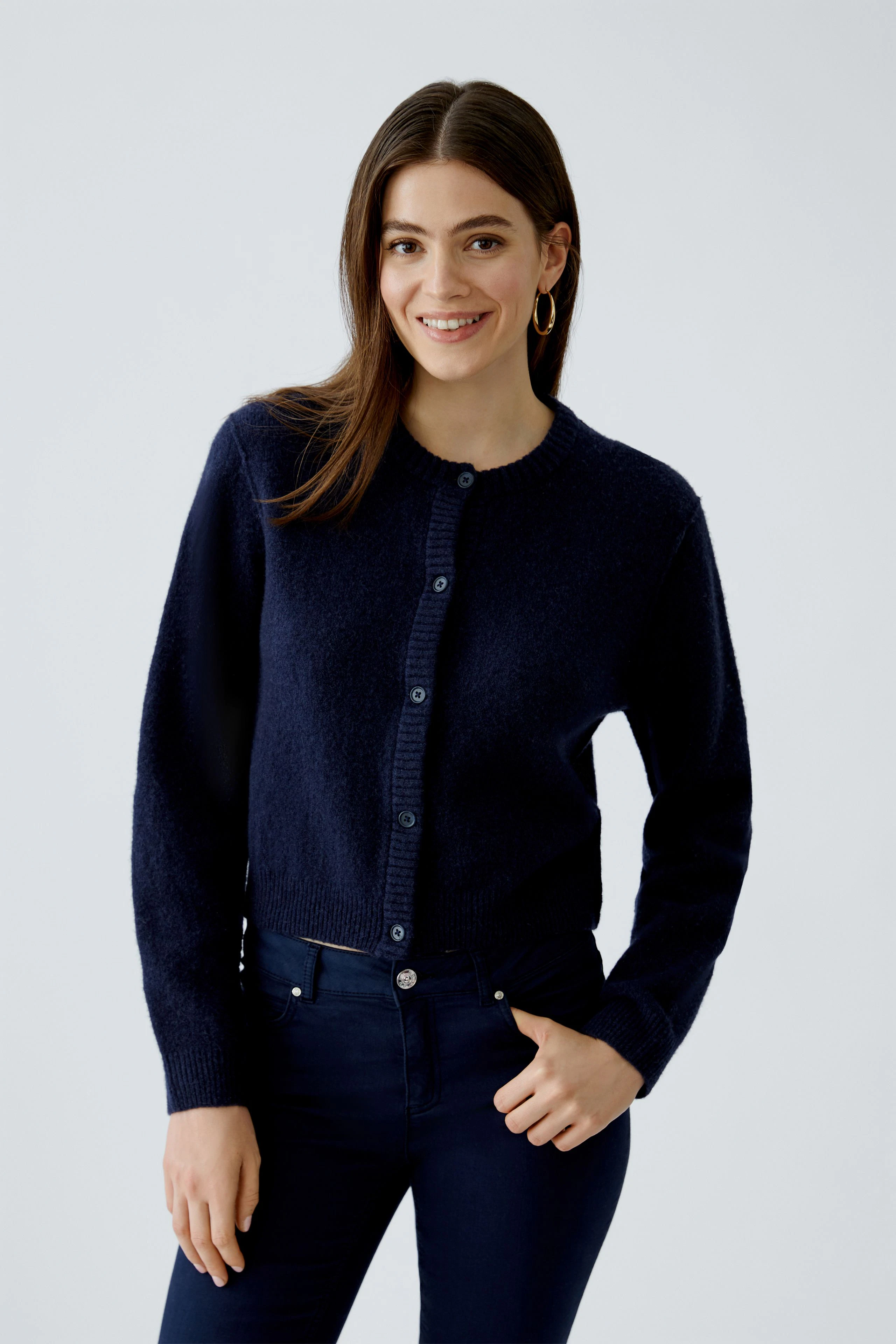 Damen-Strickjacke: Junge Frau in dunkelblauer Strickjacke mit Knöpfen und lässigen Jeans lächelt.