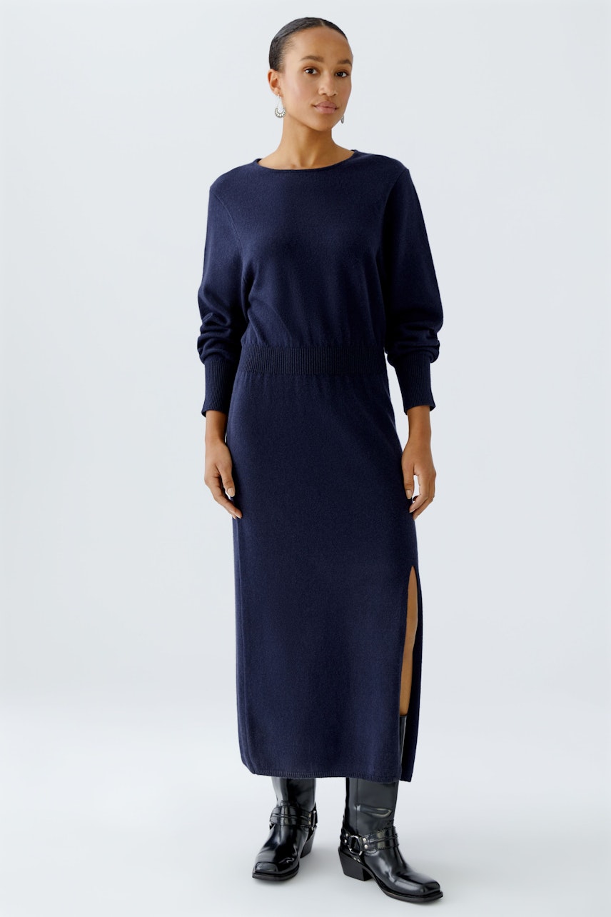 Damen-Strickkleid: Frau in dunkelblauem Strickkleid mit seitlichem Schlitz und lässigen Stiefeln.