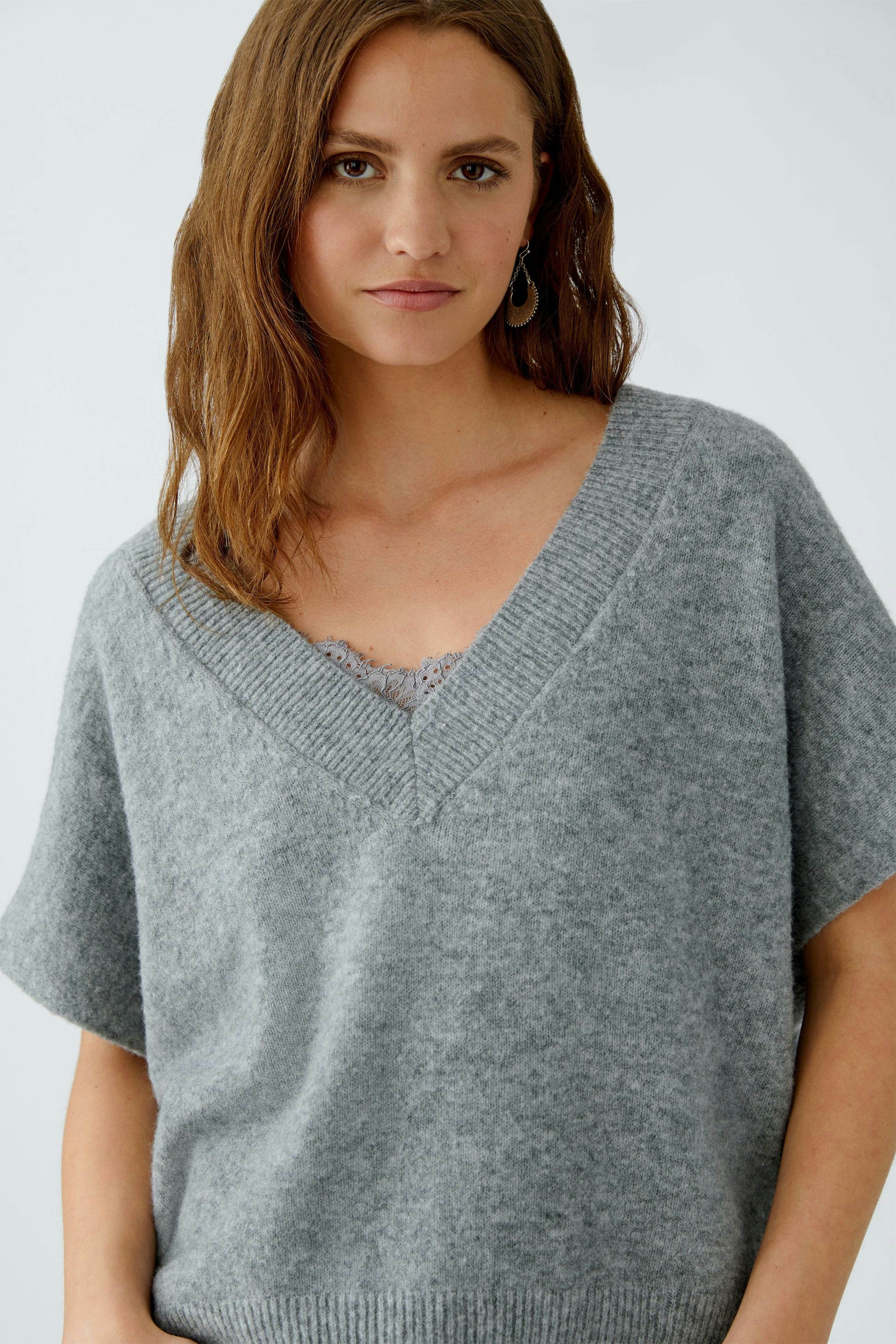 Damen-Pulunder: Frau in grauem, lässigem Strickpullover mit V-Ausschnitt und kurzen Ärmeln.