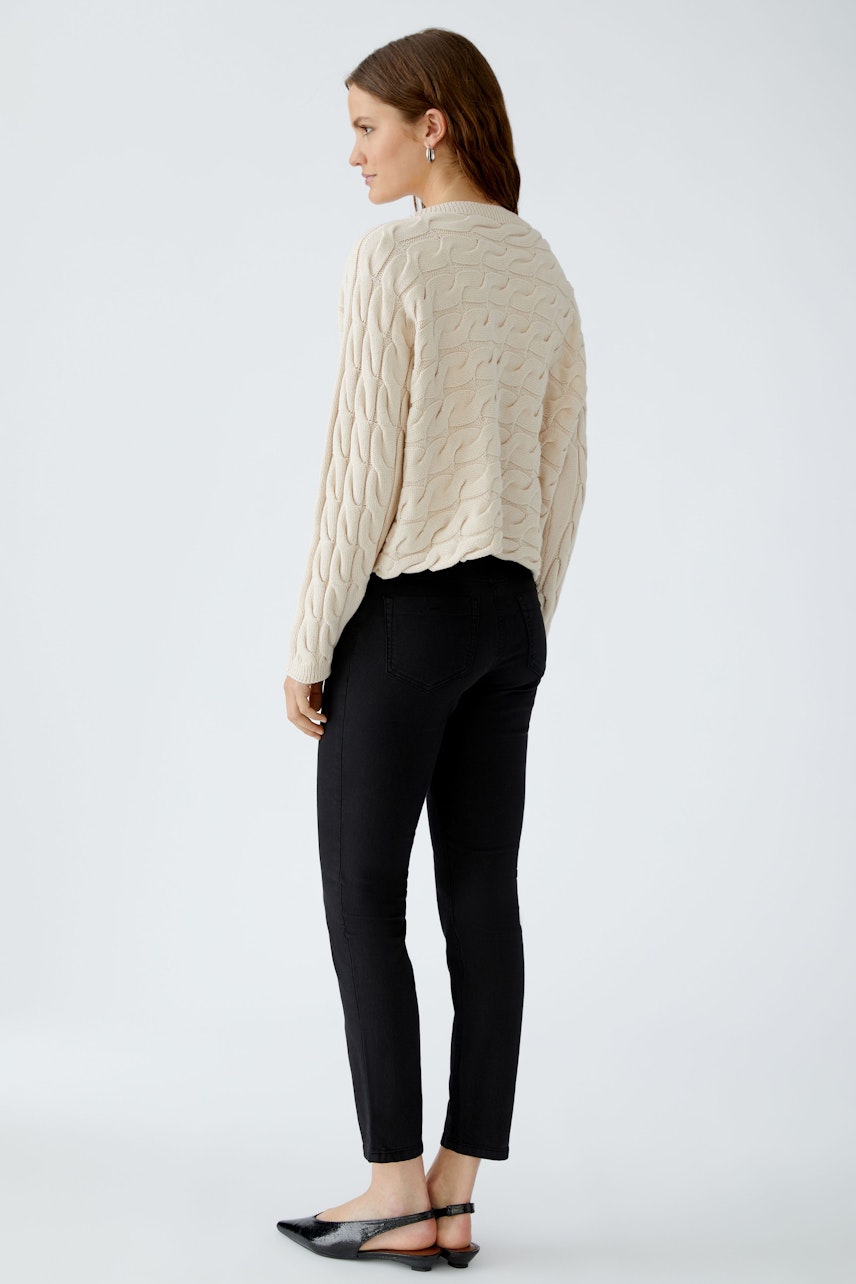 Casual women's pullover: A woman in a cream cable-knit pullover paired with black jeans.