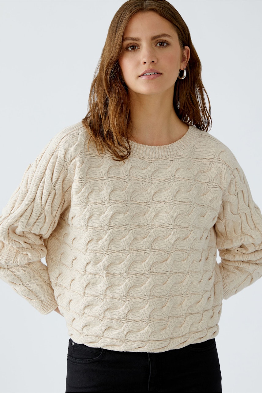 Casual women's pullover: Young woman in a cream cable-knit pullover with a relaxed fit.