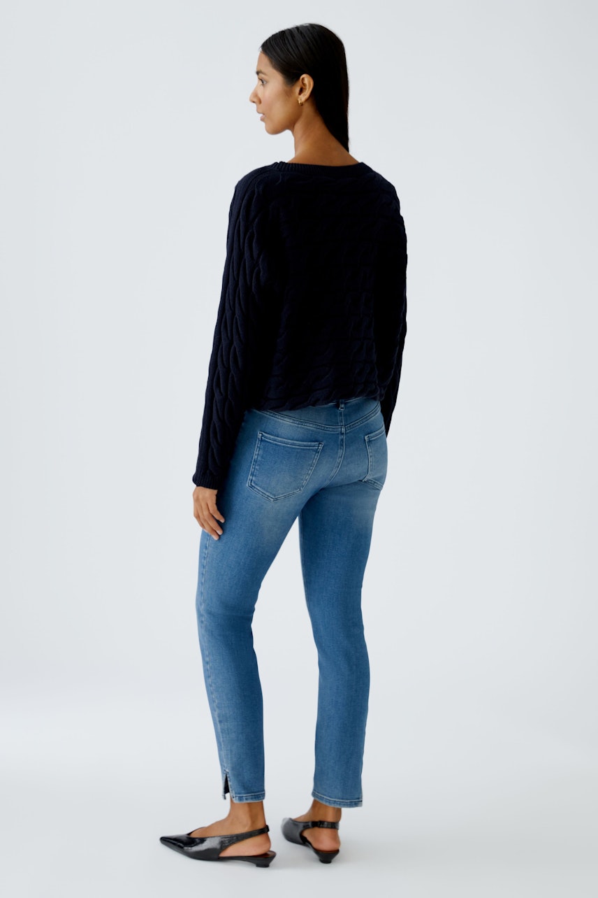 Damen-Pullover: Frau in schwarzem, strukturiertem Pullover mit lässigem Schnitt und blauen Jeans.
