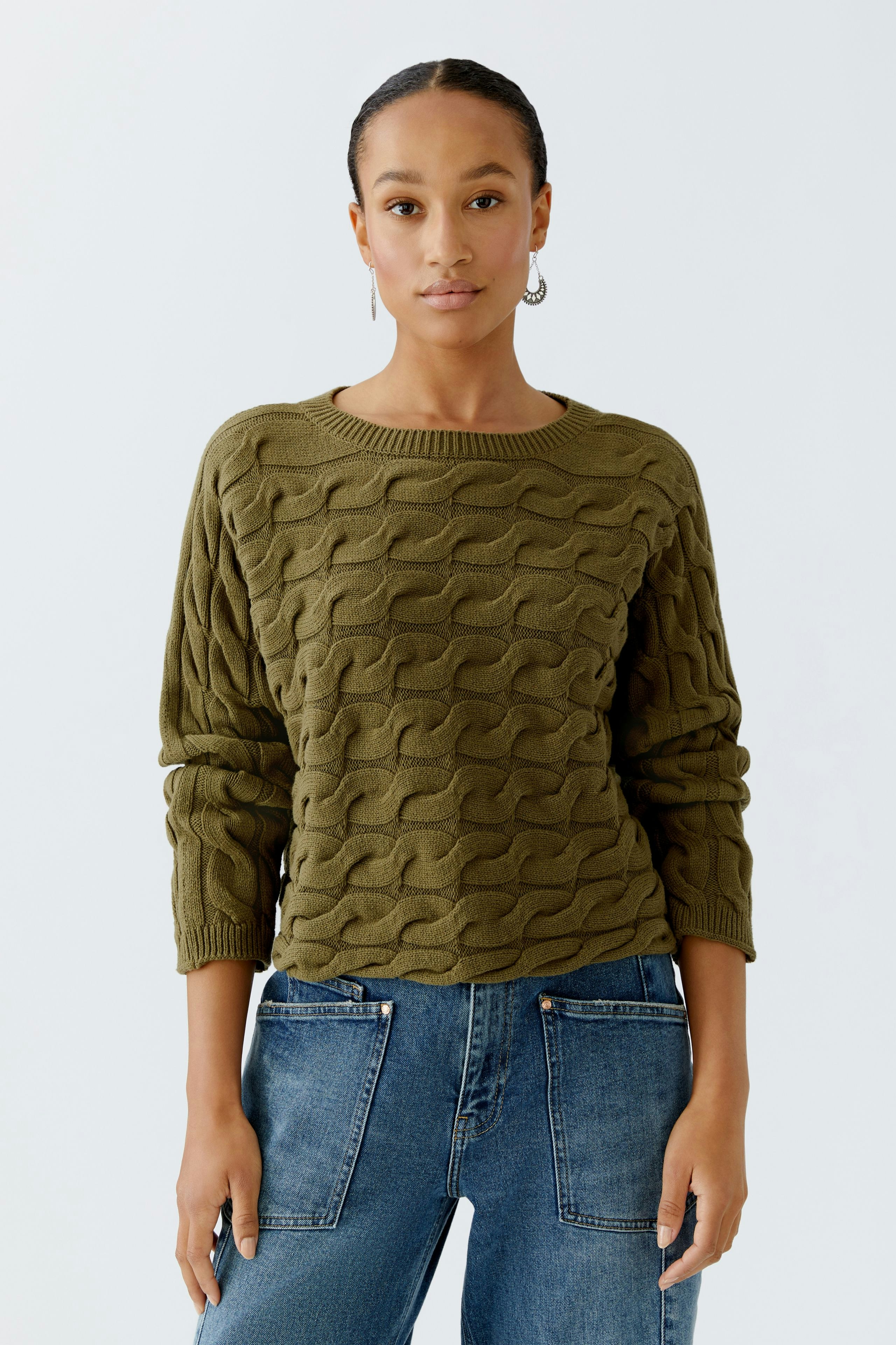 Casual women's pullover in olive green with a textured pattern, paired with blue jeans.