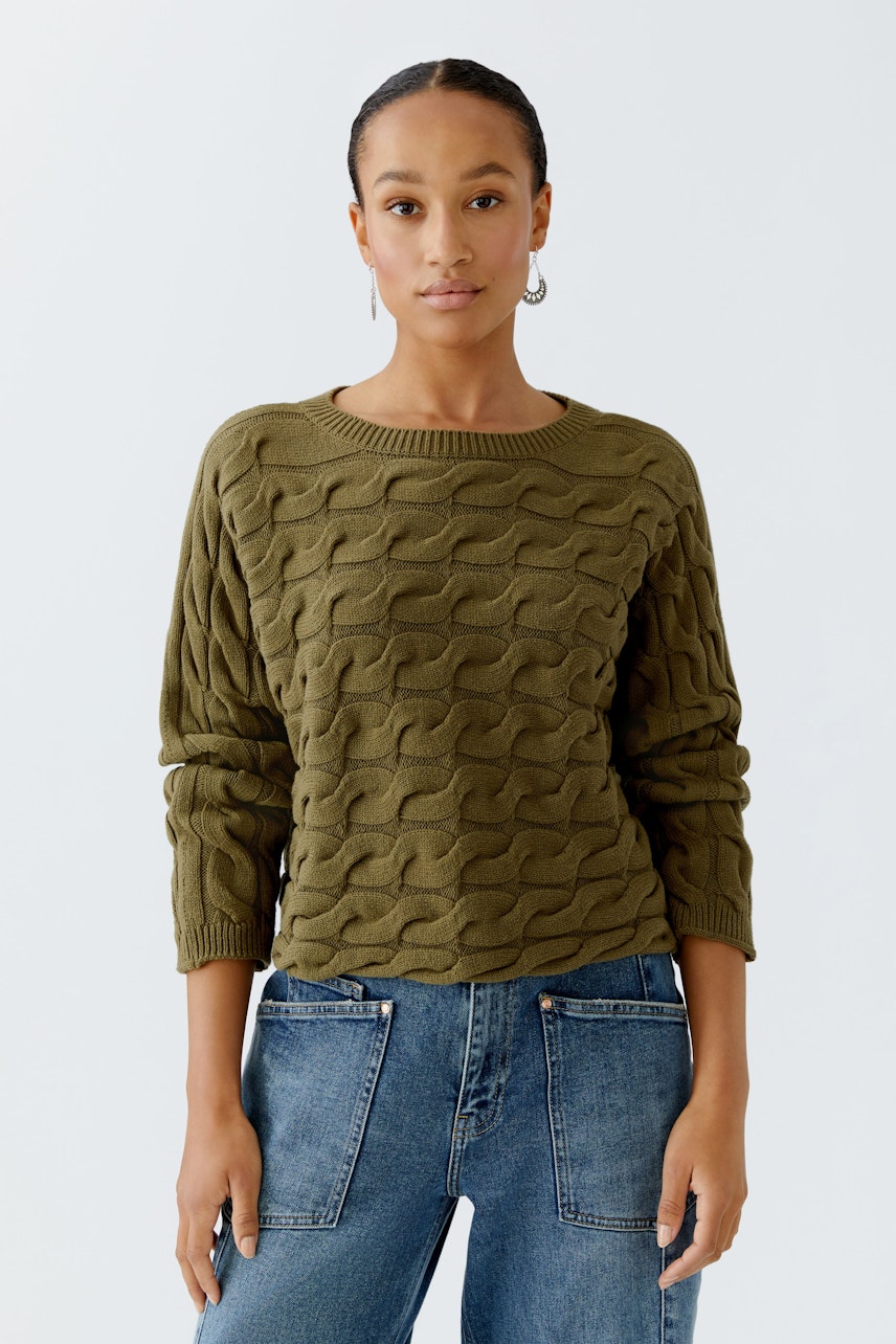 Casual women's pullover in olive green with a textured pattern, paired with blue jeans.