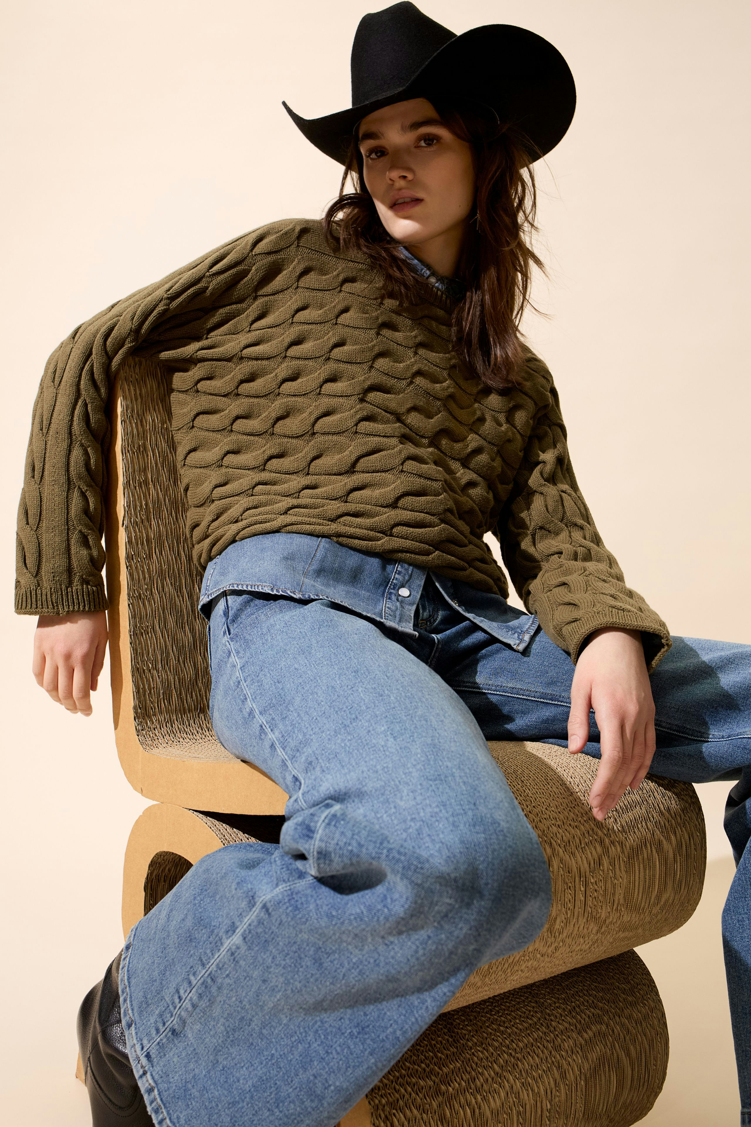 Casual women's pullover: Young woman in a textured olive pullover, paired with denim and a cowboy hat.
