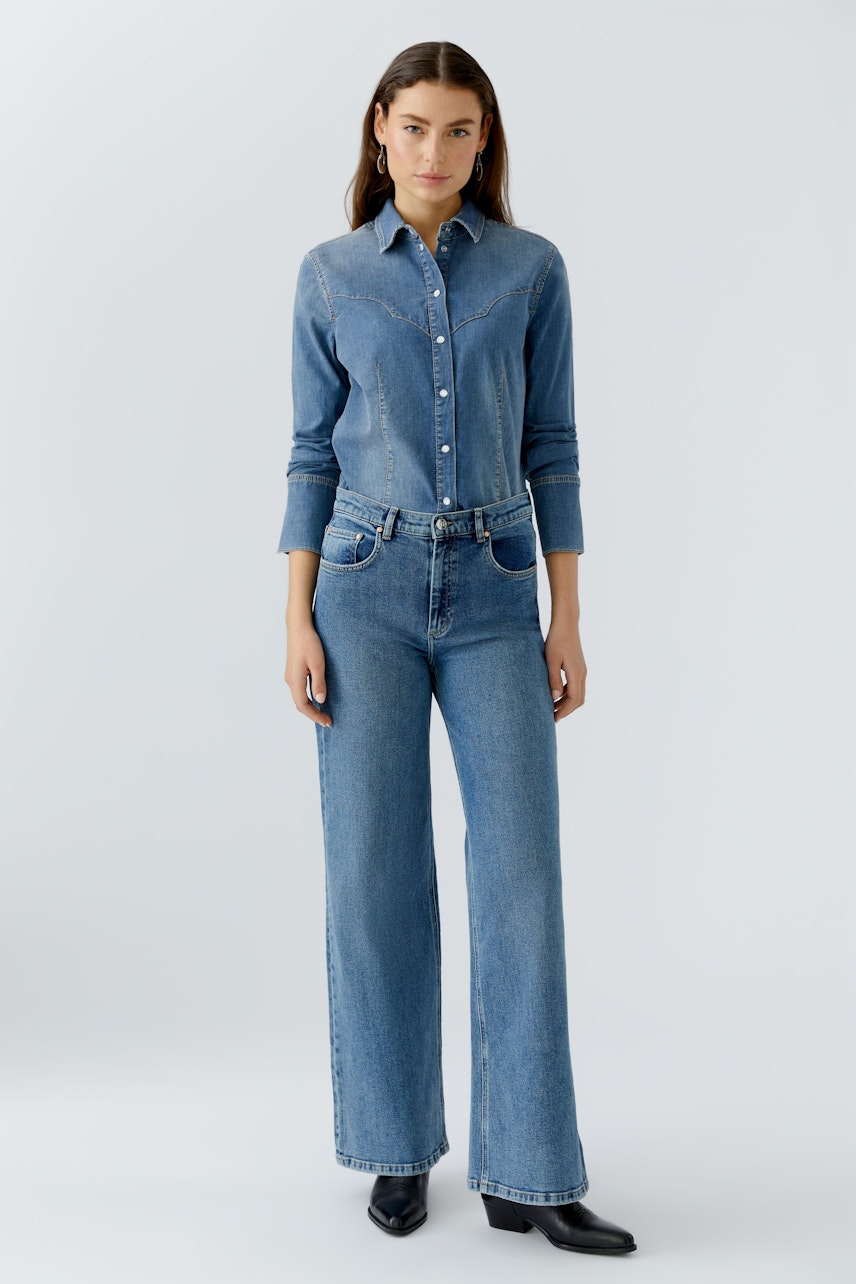 5-Pocket Hose: Junge Frau in lässiger Jeans mit weitem Bein und Hemd, steht selbstbewusst.