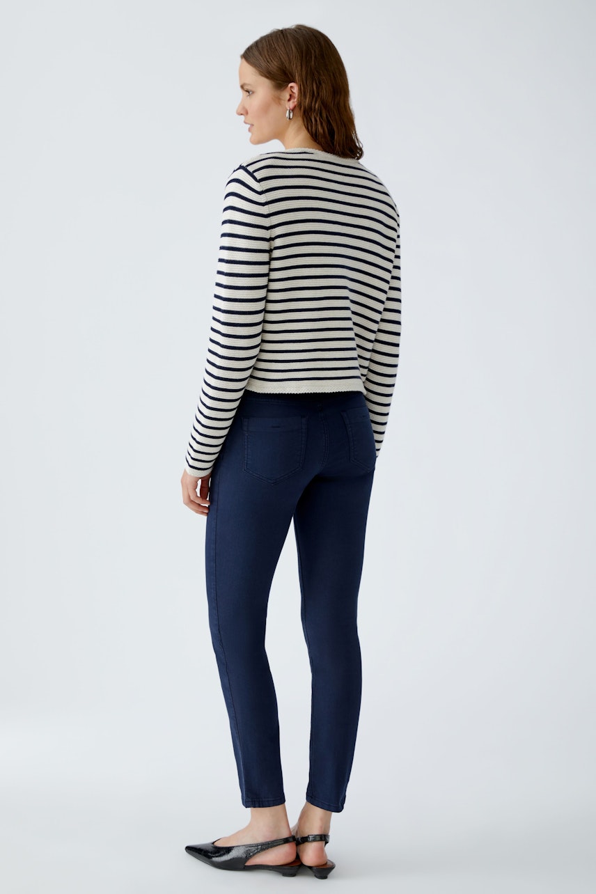 Casual women's cardigan: A woman in a striped cardigan and dark jeans stands confidently, showcasing a relaxed style.