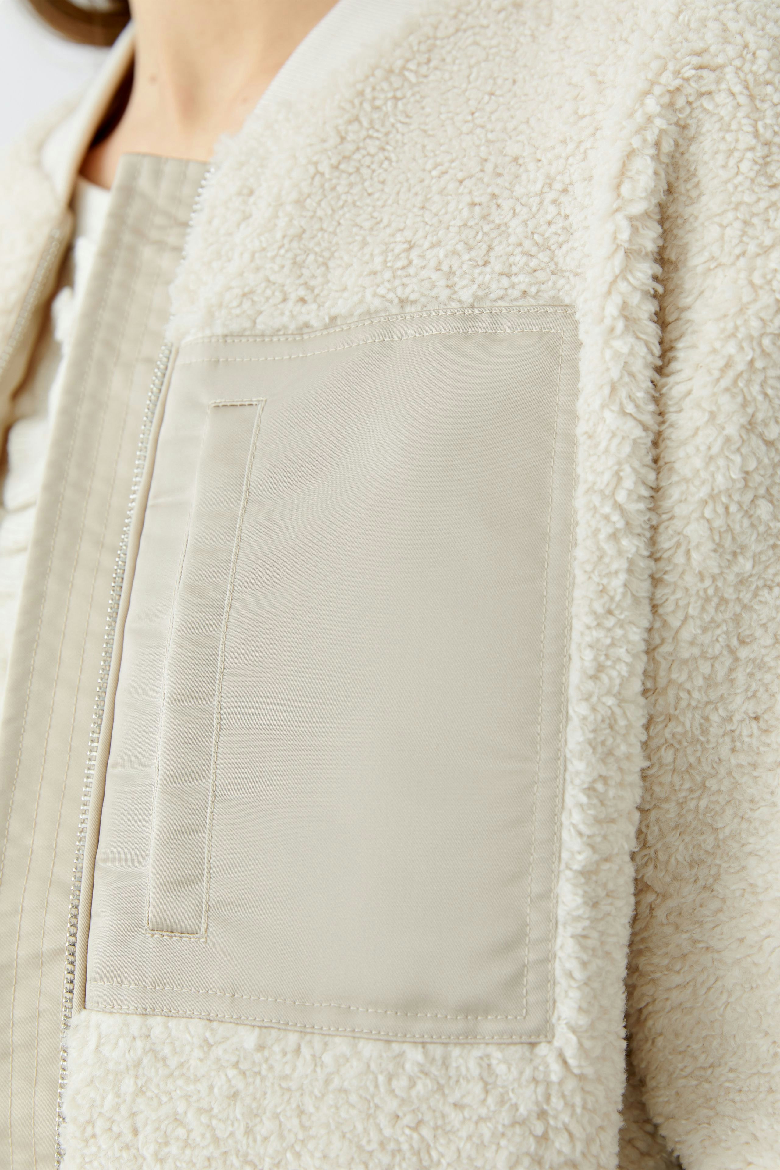 Cozy women's blouson: Close-up of a woman in a soft, cream-colored jacket with a plush texture.