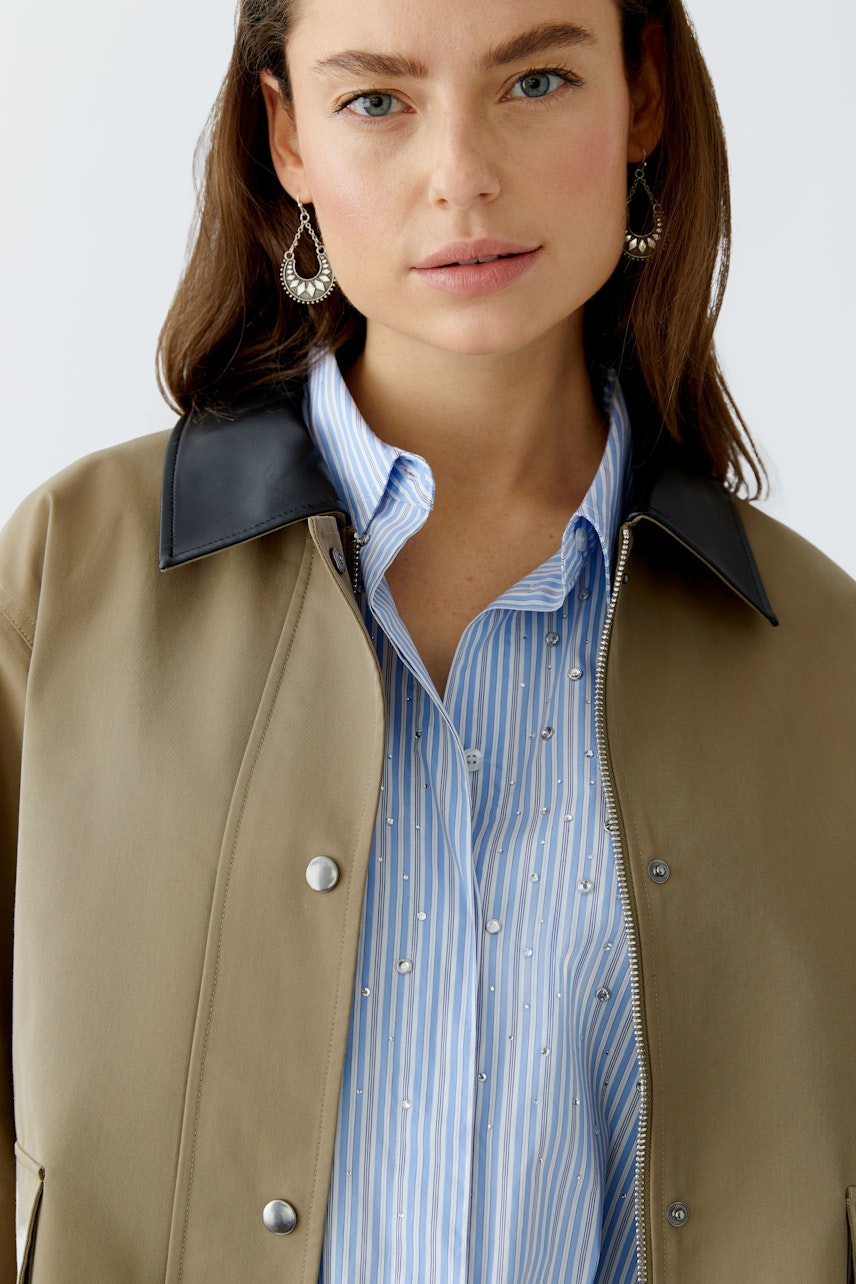 Damen-Jacke: Frau in beiger Jacke mit schwarzem Kragen und gestreifter Bluse, lässiger Look.