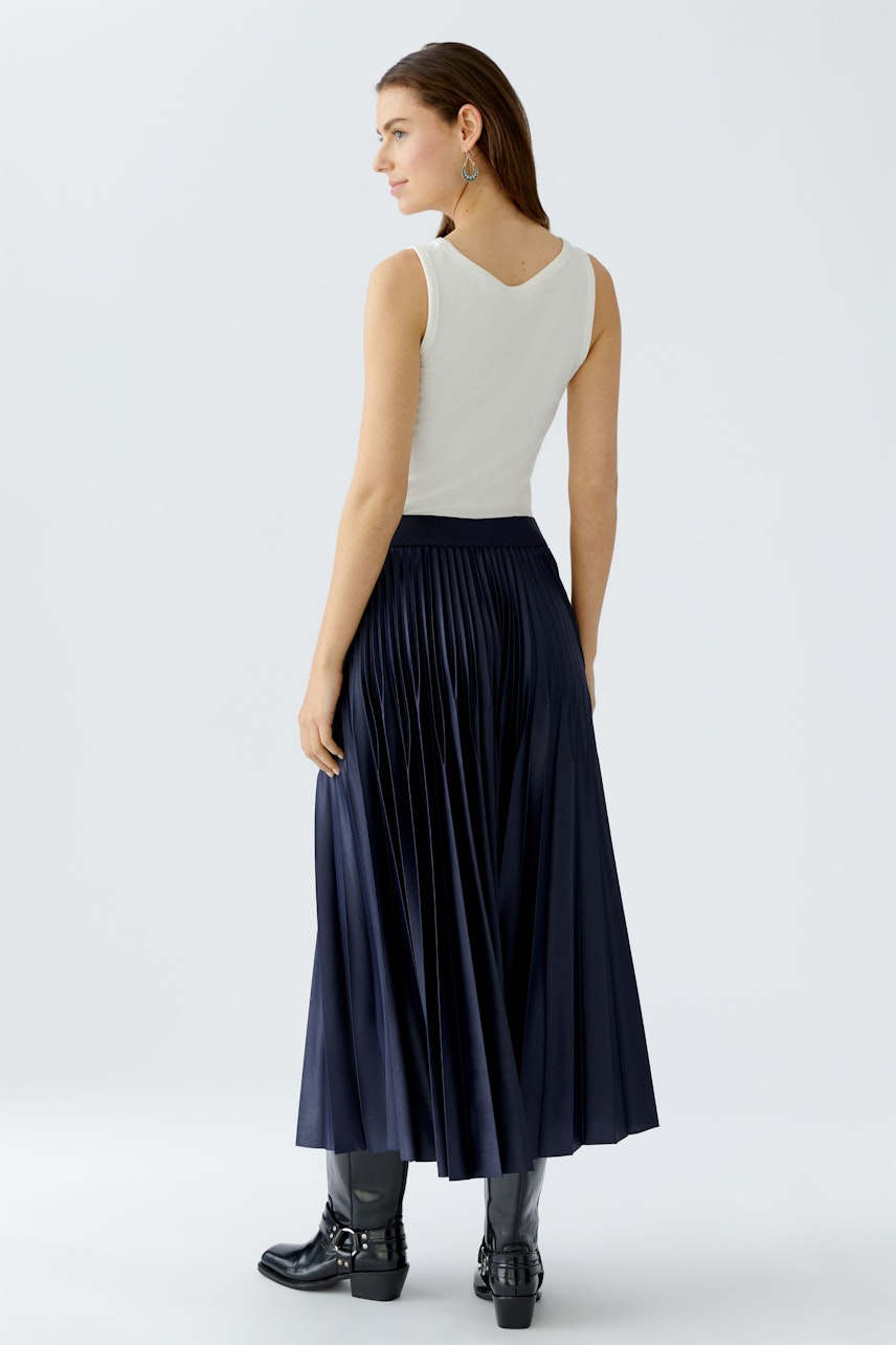 Damen Plisseerock: Frau in navyfarbenem Plisseerock mit schlichter Bluse und modischen Stiefeln.