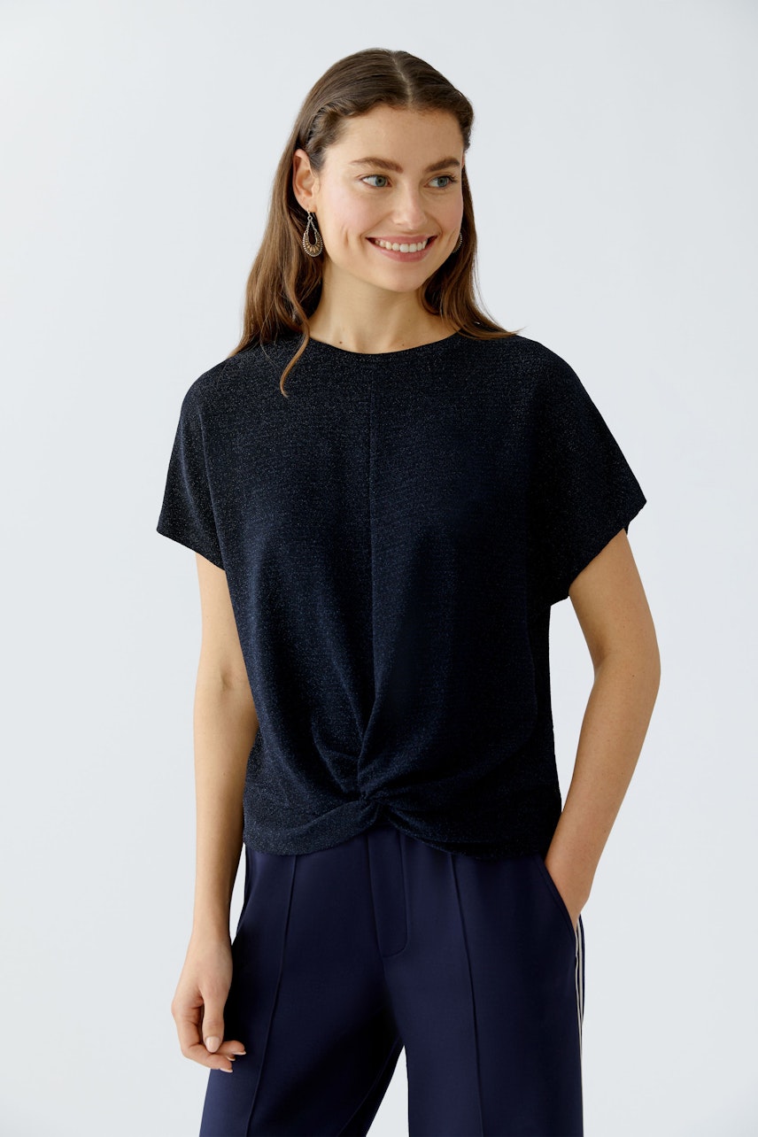 Casual women's T-shirt: Smiling woman in a black top with a knotted front, paired with stylish trousers.