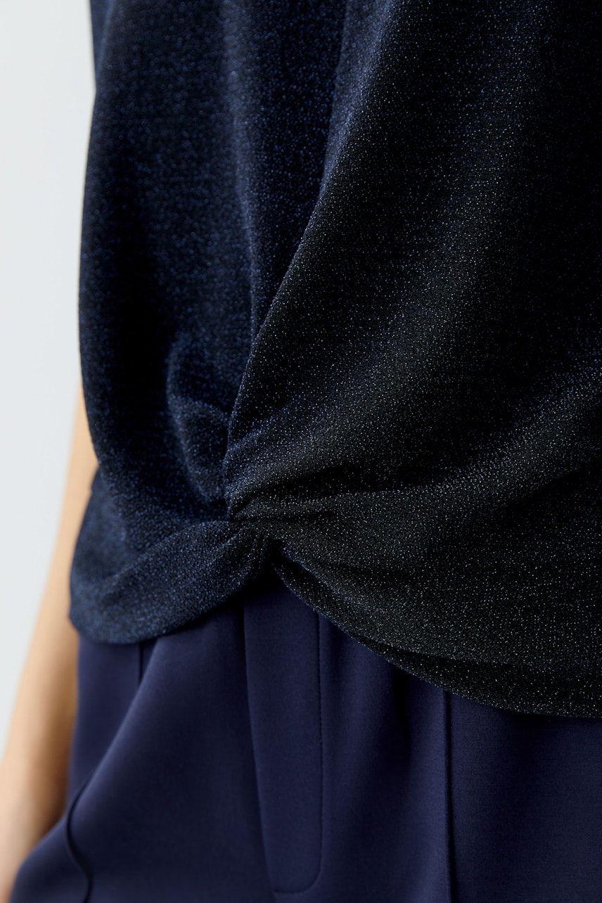 Casual women's T-shirt: Close-up of a woman wearing a dark, shiny top with a knotted detail.