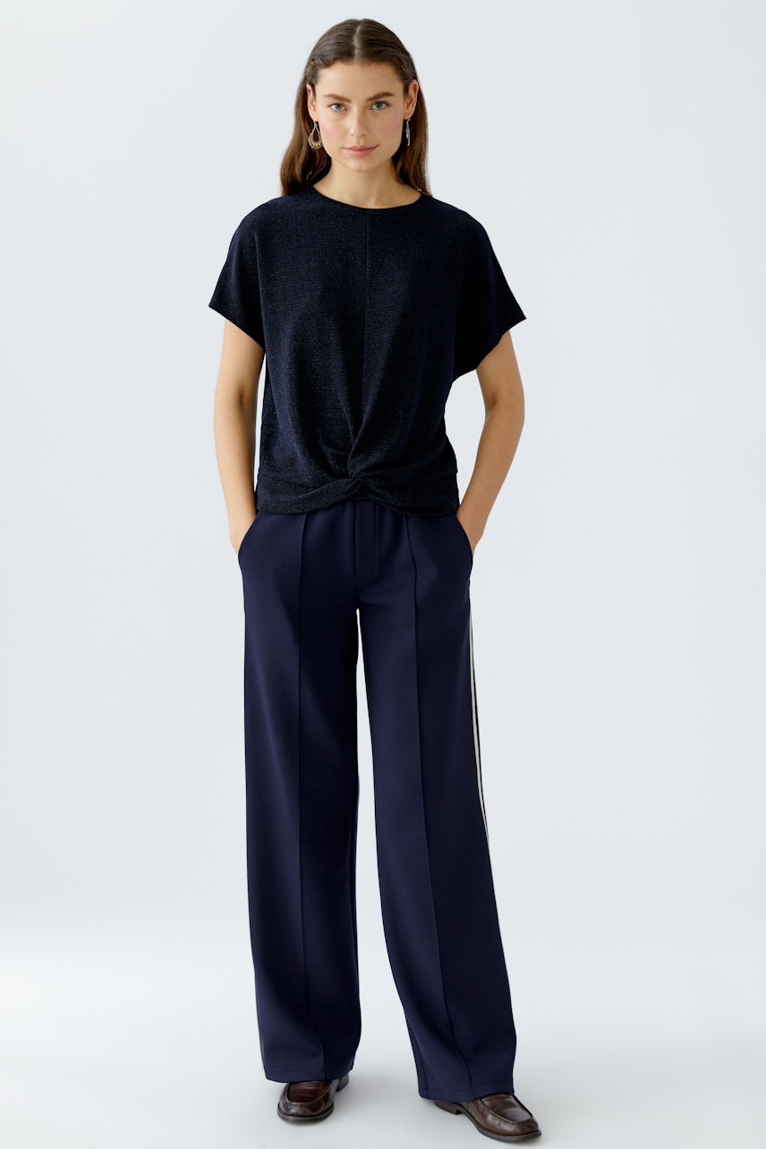Casual women's T-shirt: Young woman in a dark top with a knotted front, paired with wide trousers.