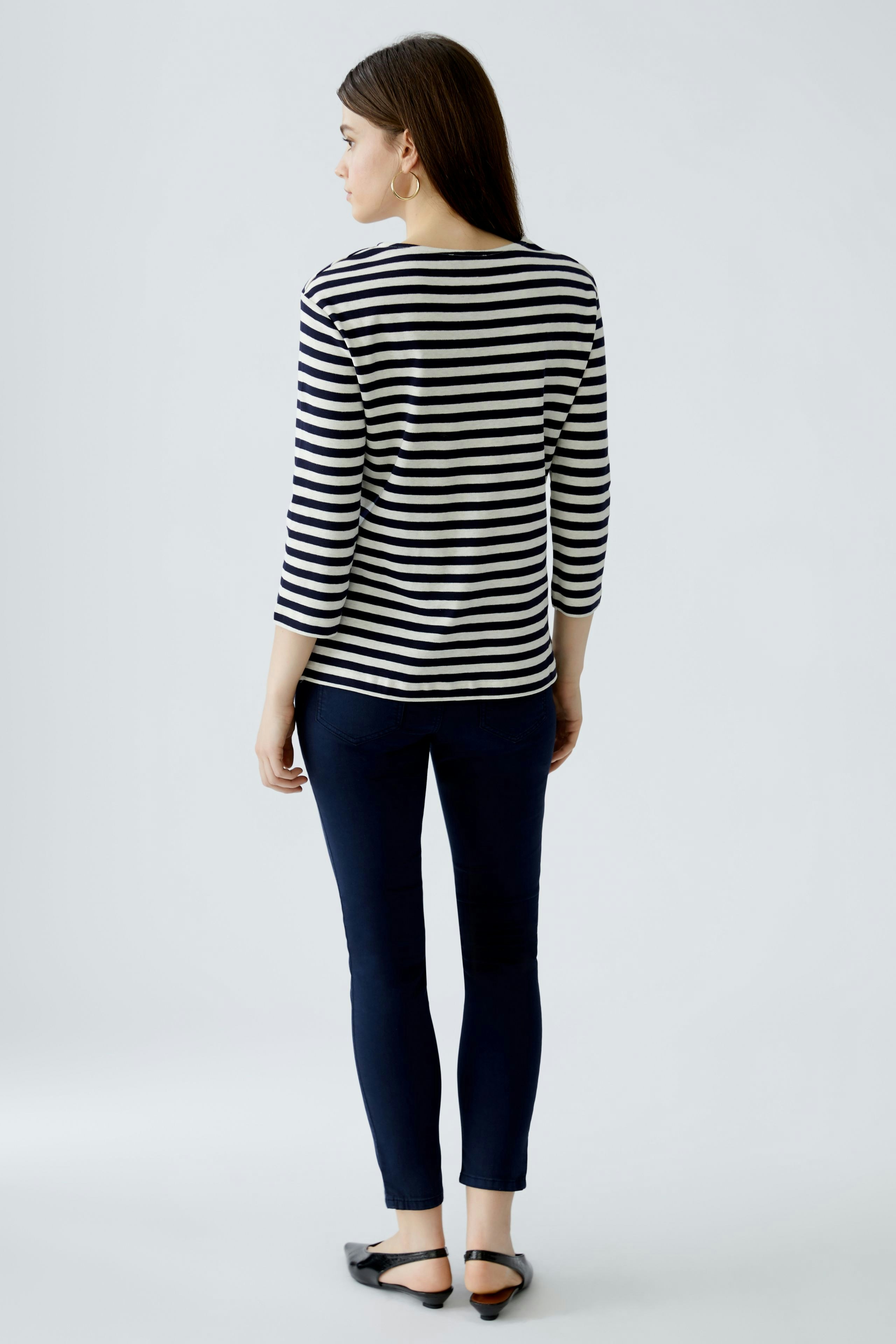 Casual women's T-shirt: Young woman in a striped top and dark pants, viewed from the back.