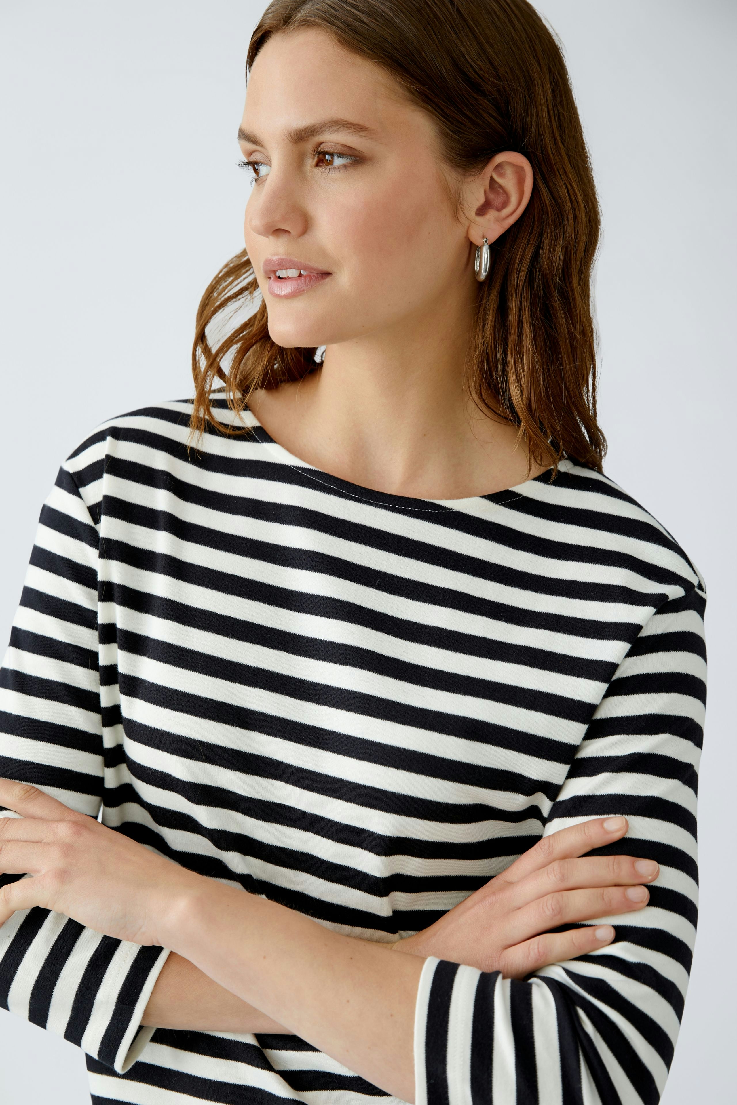 Casual women's T-shirt: Young woman in a black and white striped top, arms crossed, smiling.