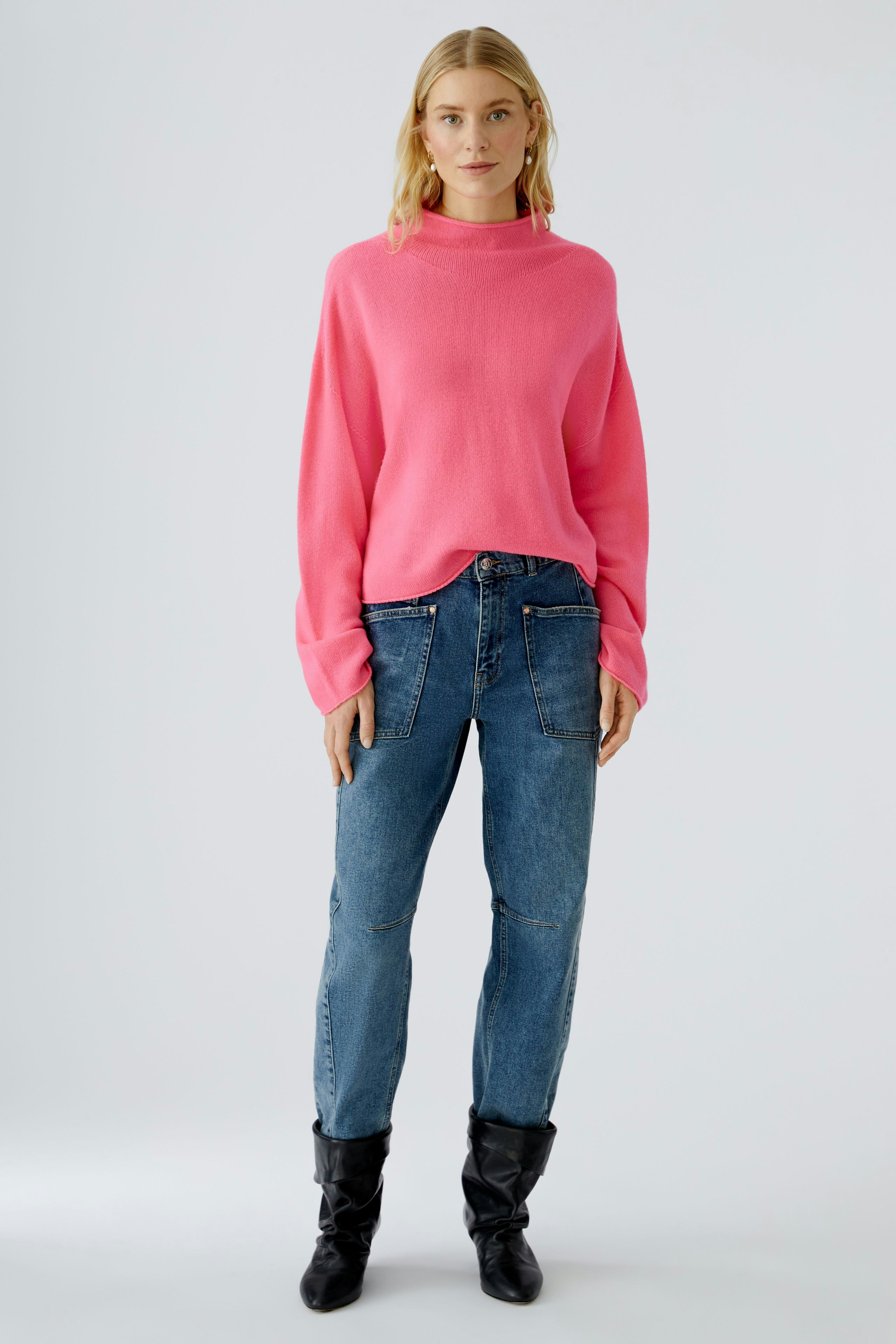 Damen-Pullover in leuchtendem Pink, lässig kombiniert mit Jeans und Stiefeln, getragen von einer Frau.
