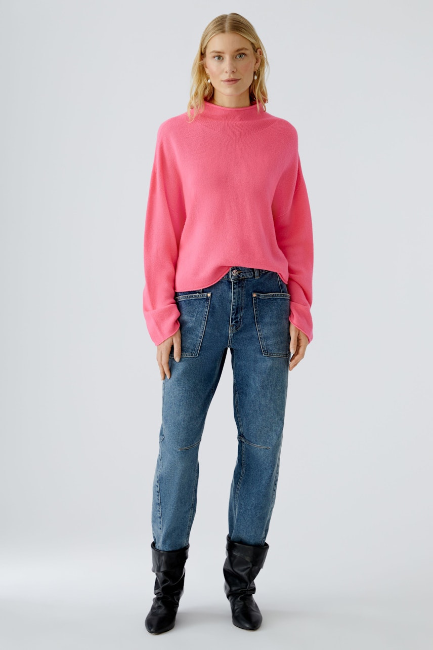 Damen-Pullover in leuchtendem Pink, lässig kombiniert mit Jeans und Stiefeln, getragen von einer Frau.