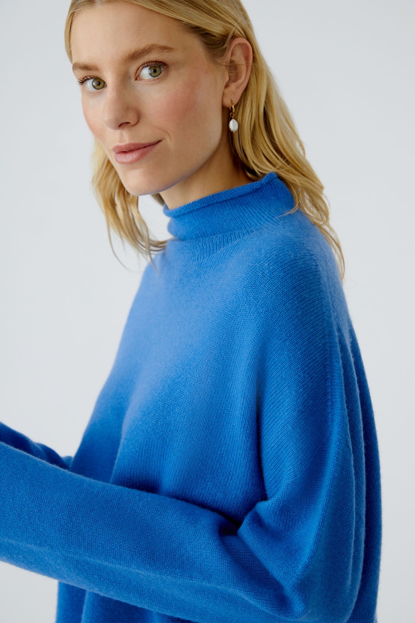 Modern women's pullover: A woman in a vibrant blue pullover with a high neck, smiling softly.