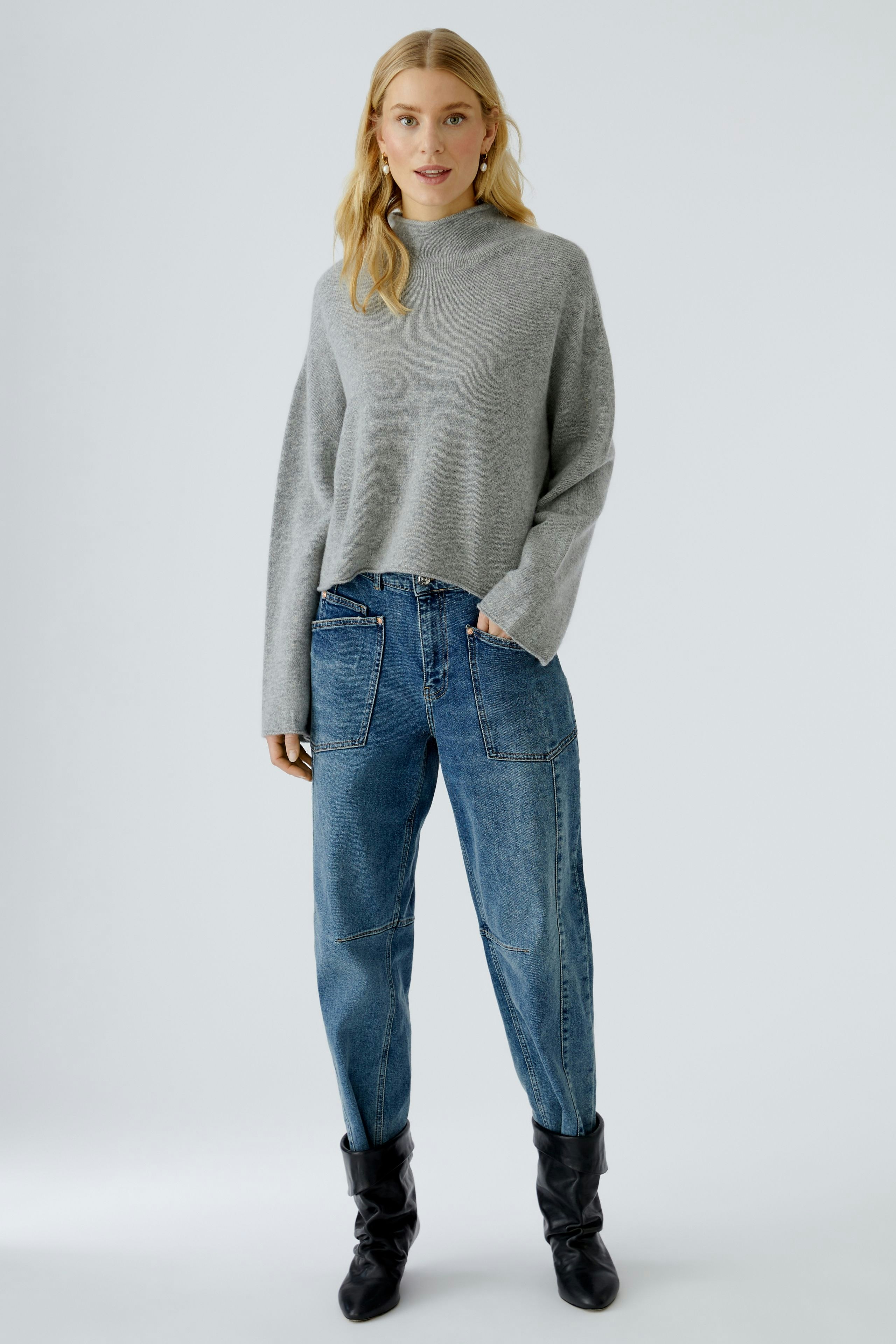 Bequemer Damen-Pullover: Frau in grauem, lässigem Pullover mit weitem Schnitt und Jeans.