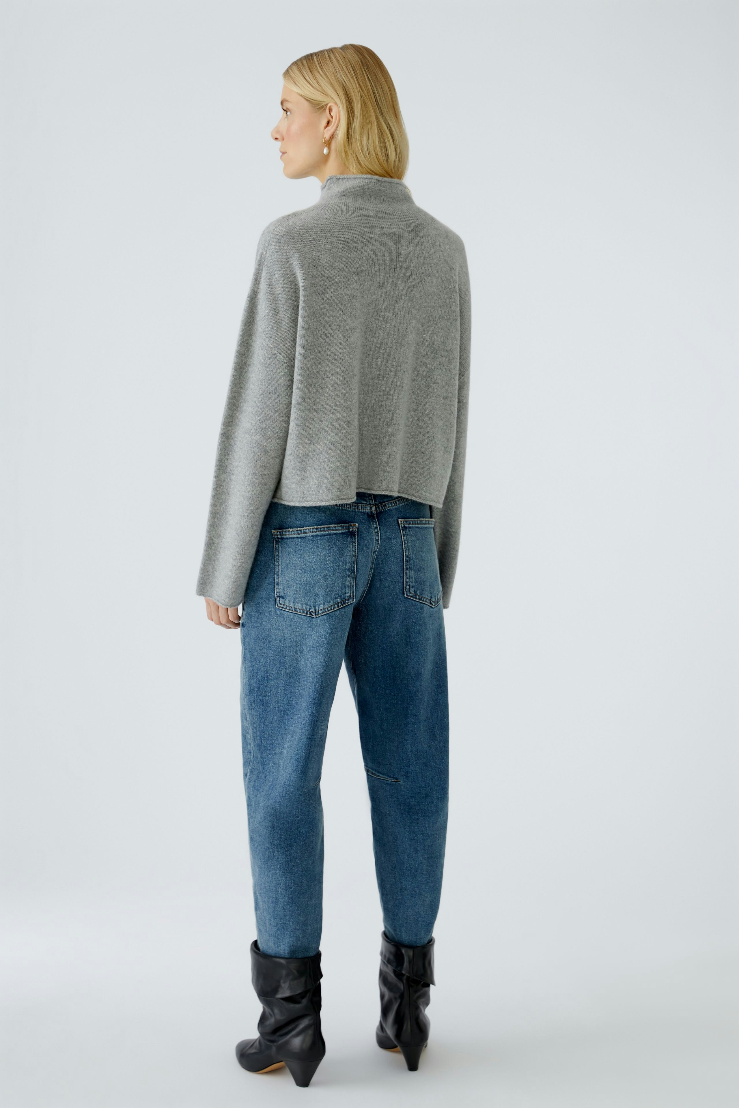 Damen-Pullover: Frau in grauem, lässigem Strickpullover mit lockerer Passform und Jeans.