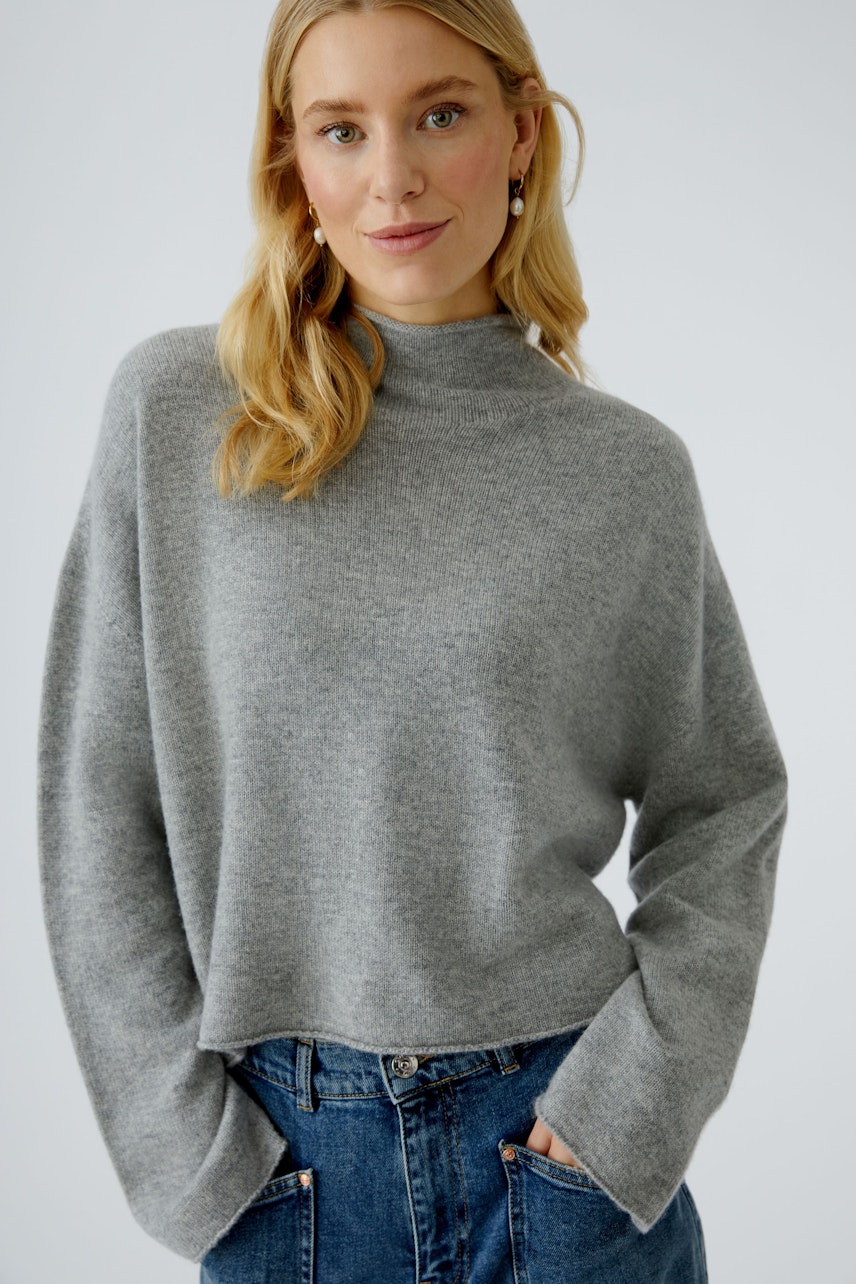 Bequemer Damen-Pullover: Frau in grauem, lässigem Strickpullover mit hohem Kragen und weitem Schnitt.