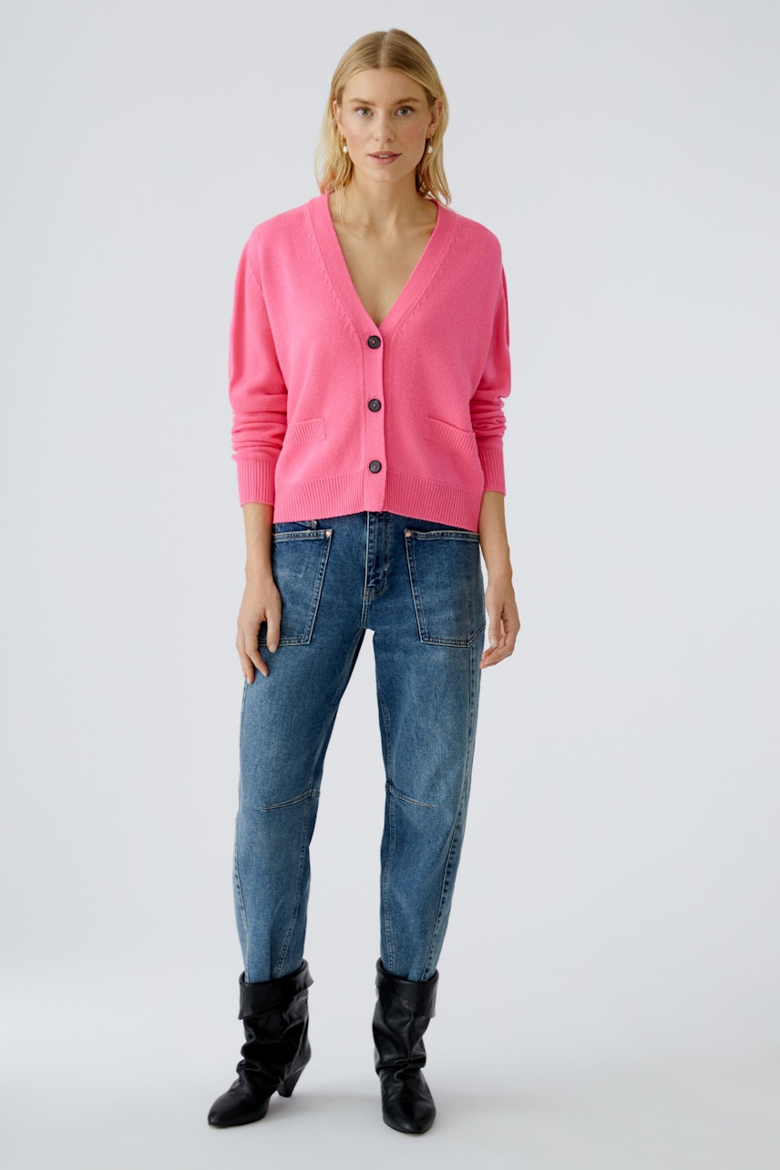 Bequeme Damen-Strickjacke: Frau in pinker Strickjacke mit V-Ausschnitt und Knöpfen, kombiniert mit Jeans.